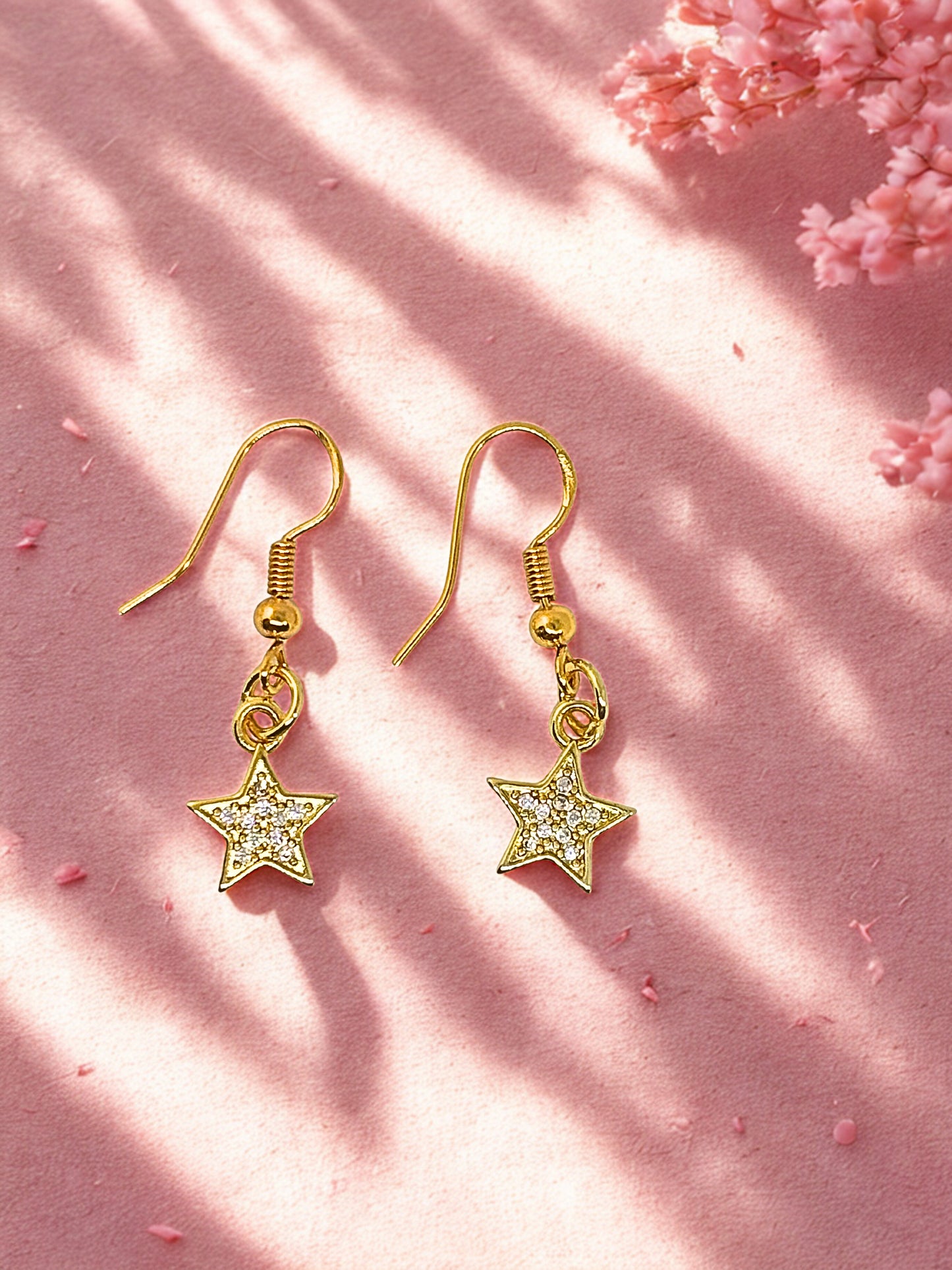 Gold star-shaped earrings on a pink background with cherry blossoms.