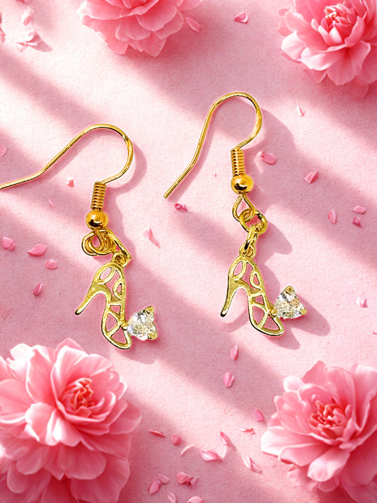 Gold high heel shoe earrings with clear gemstones on a pink floral background