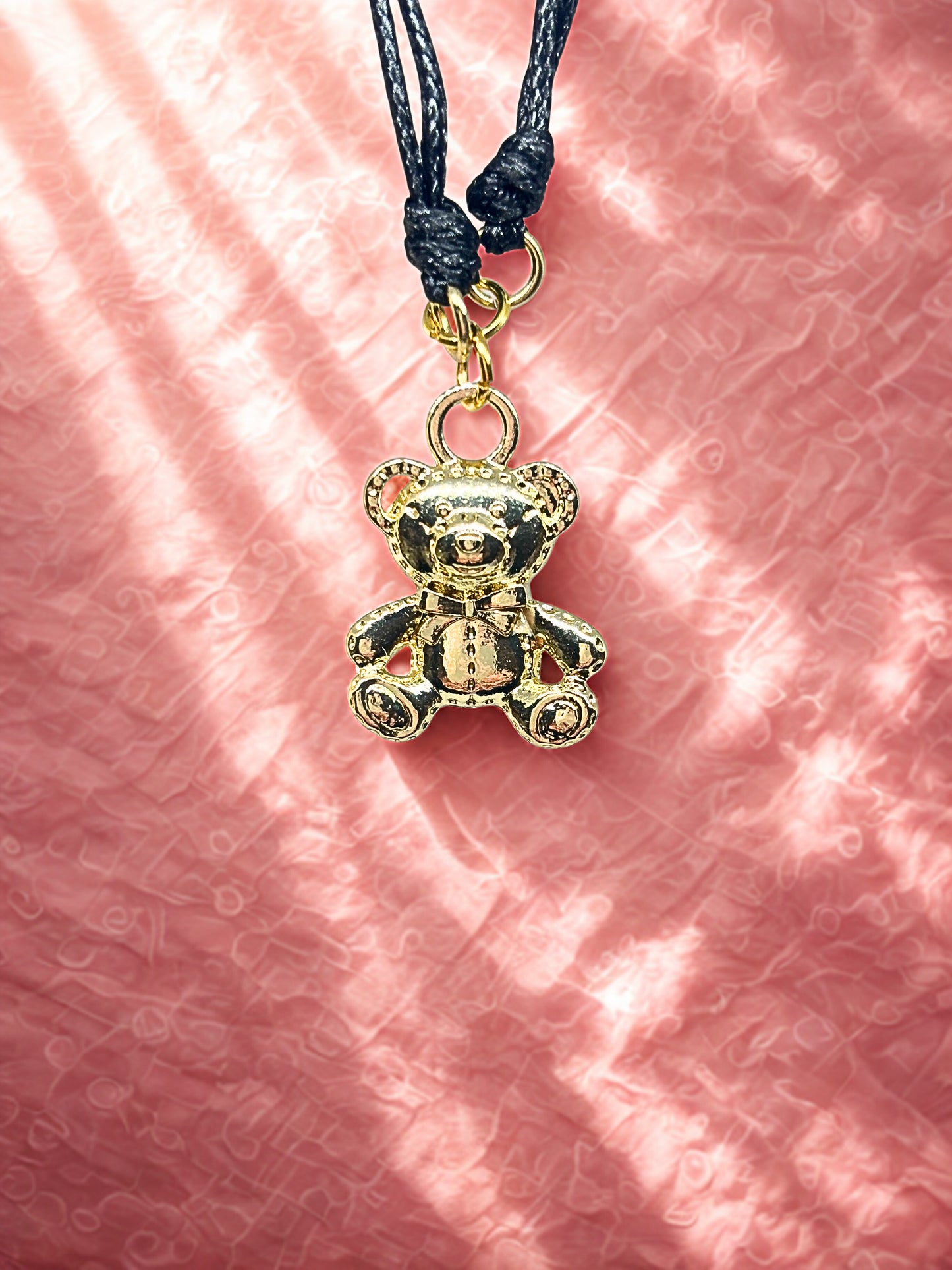Gold teddy bear charm on a pink textured background