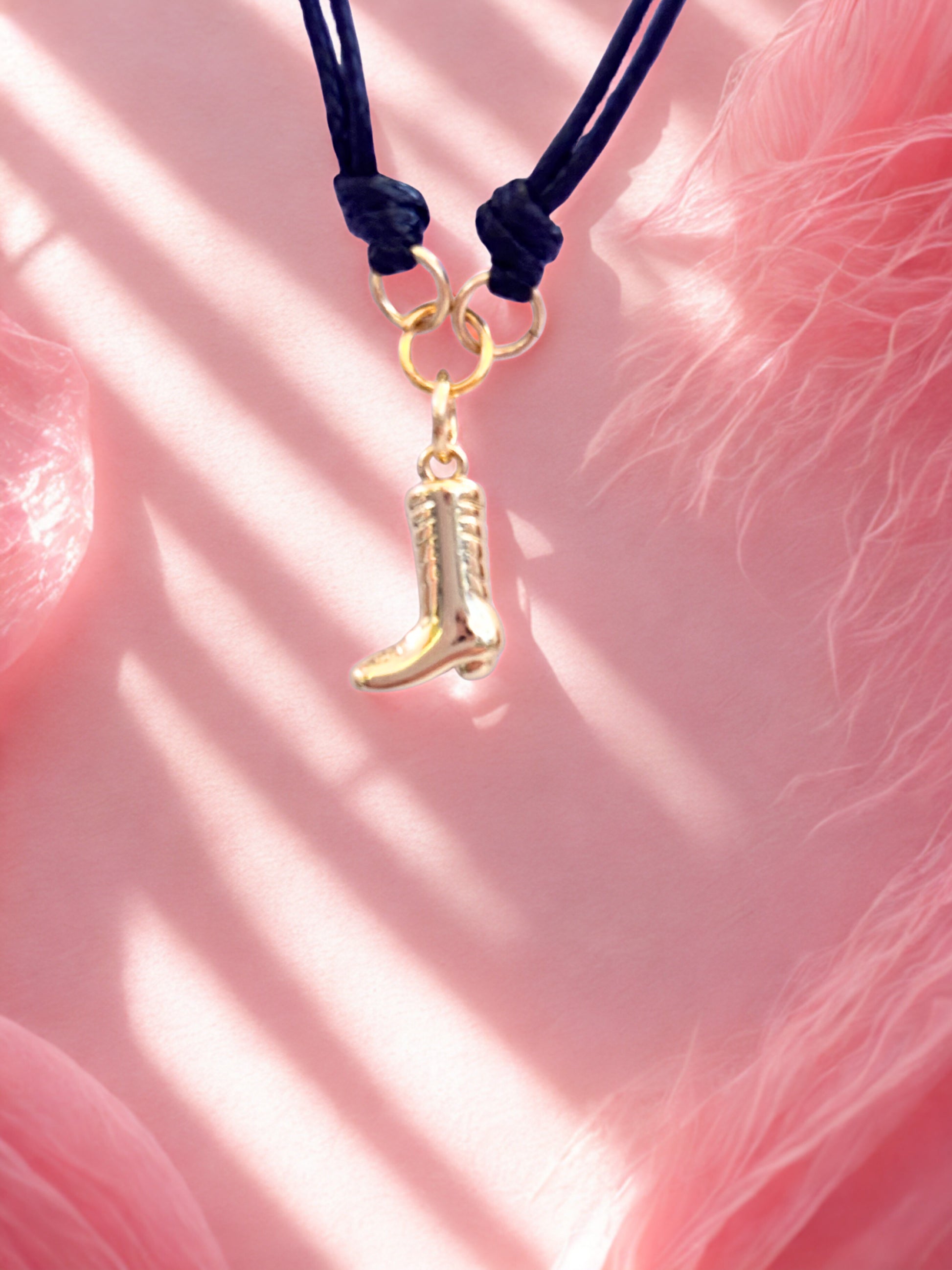 Gold boot charm on a black cord against a pink feathered background