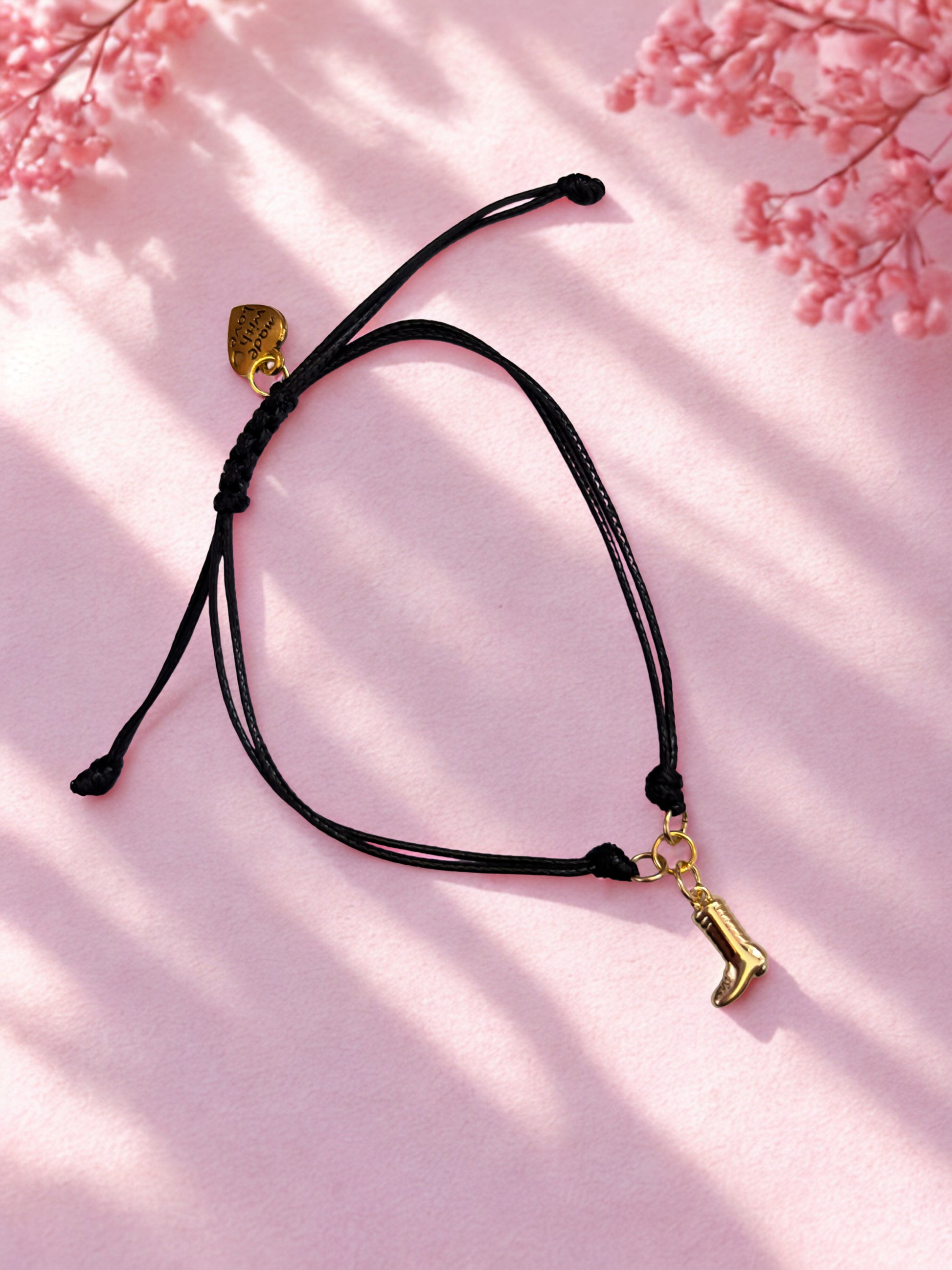 Black cord bracelet with gold boot charm on a pink floral background