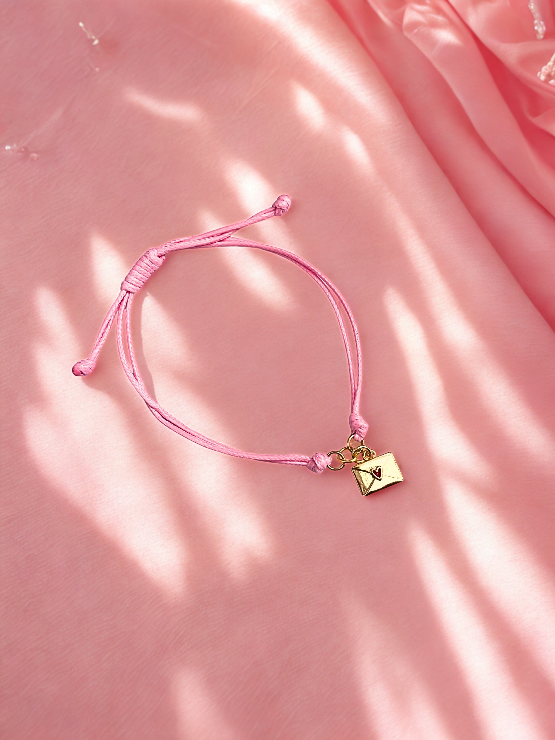 Pink bracelet with a gold envelope charm on a pink fabric background
