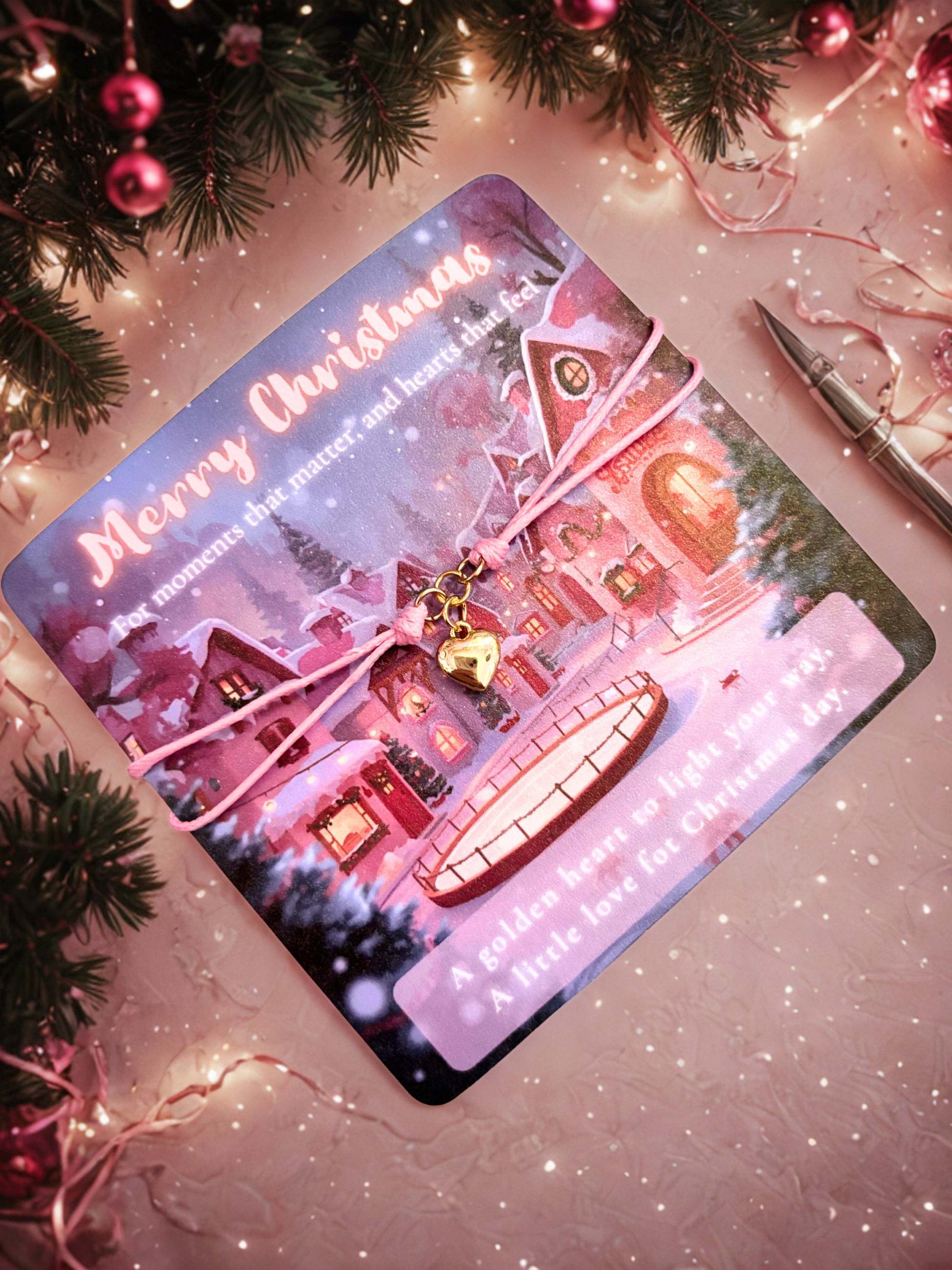 Christmas-themed card with a gold heart charm bracelet and a festive village design on a decorative surface with lights and tree branches.