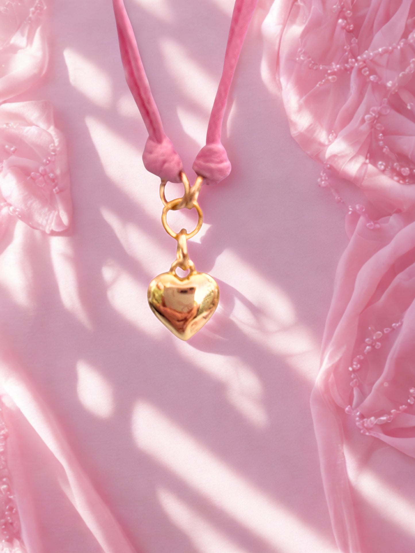 Gold heart-shaped charm on a pink cord against a pink floral background