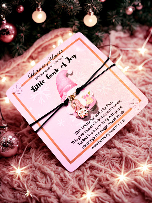 Decorative card with a pink gonk gnome charm on a textured surface with Christmas decorations.