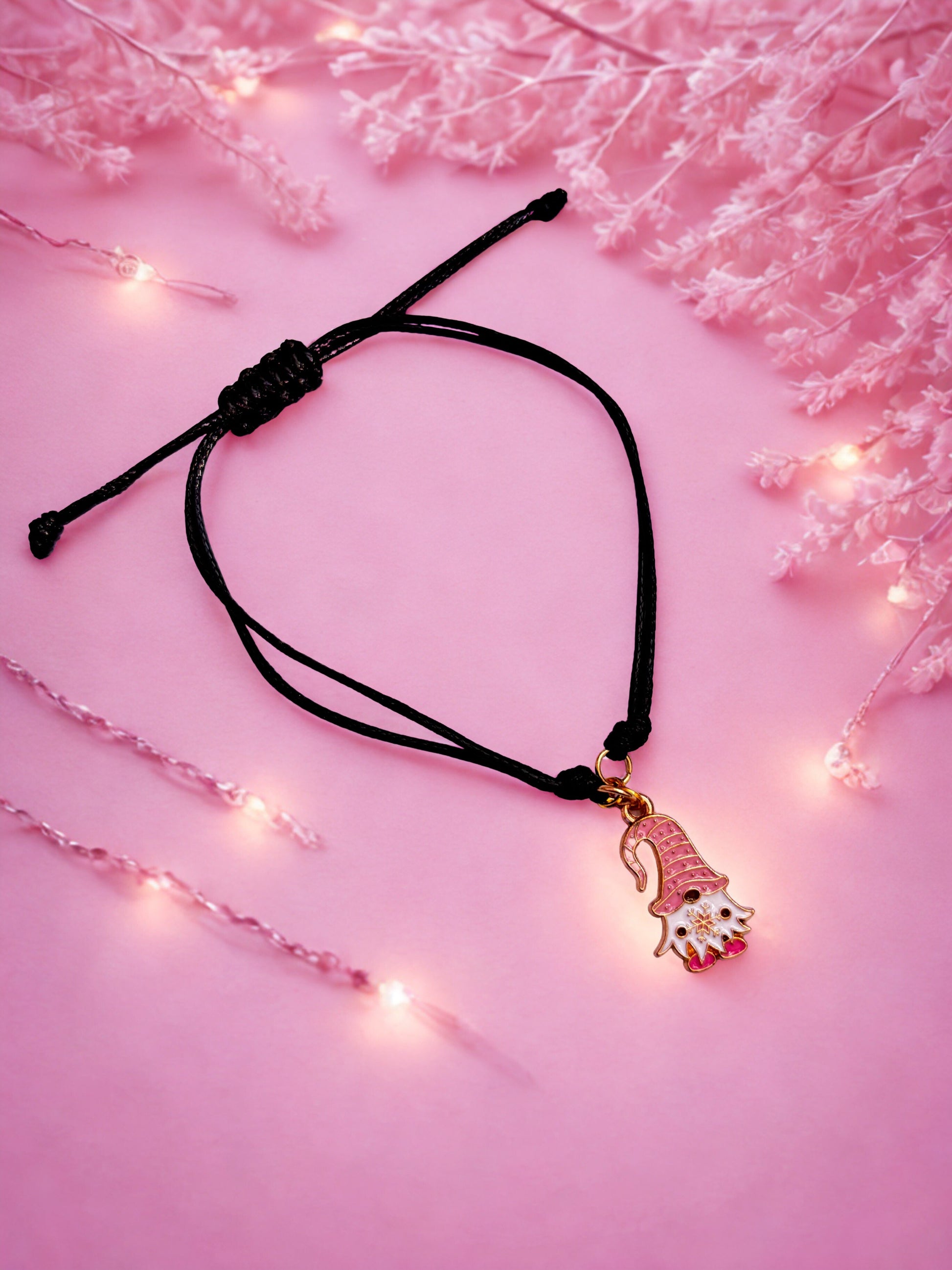Black cord bracelet with a gonk gnome charm on a pink background with fairy lights