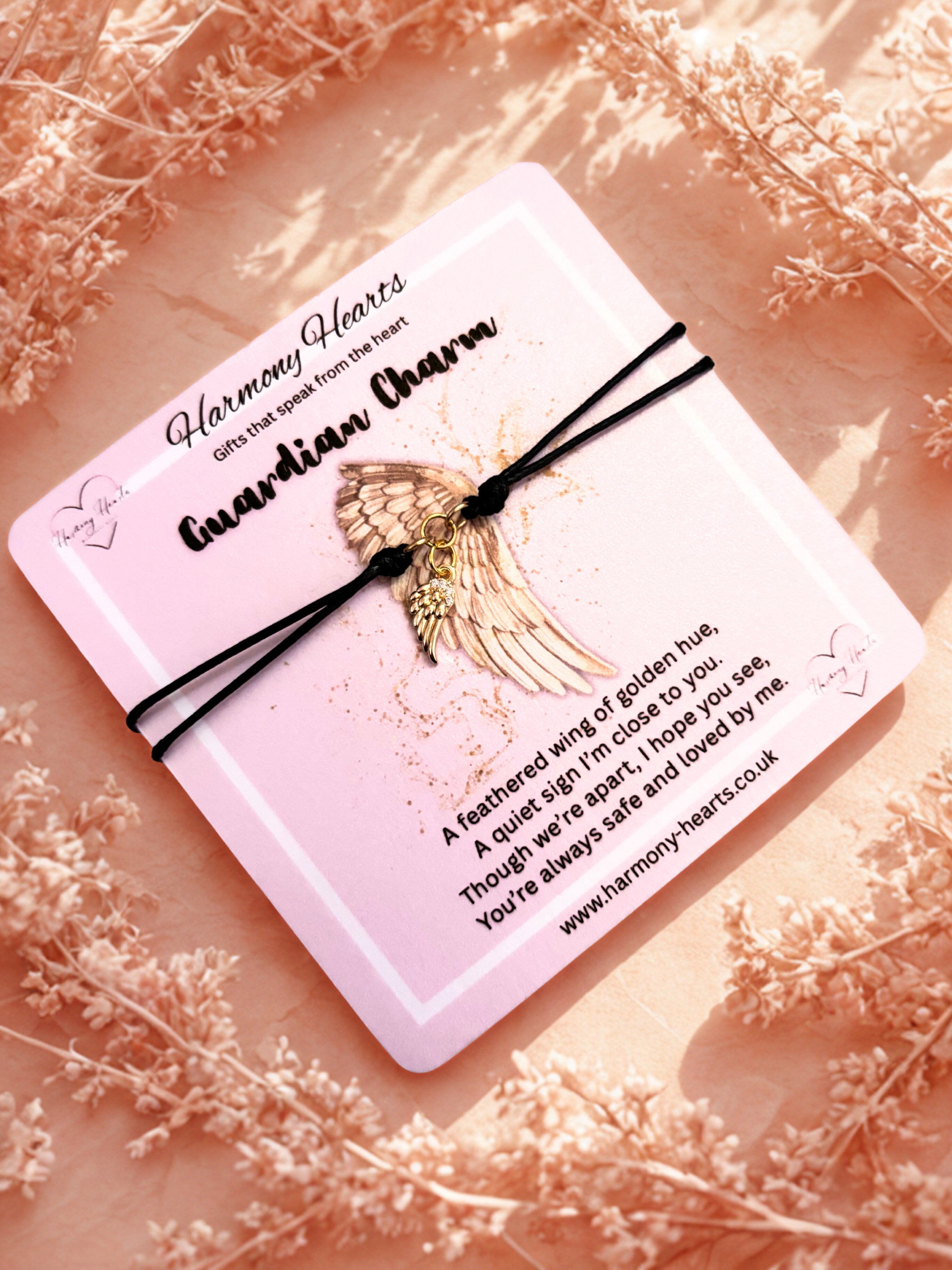 Guardian Charm bracelet with angel wing design on a pink card with text, surrounded by dried flowers.