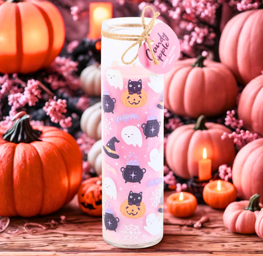 Pink candle with Halloween-themed design surrounded by pumpkins and candles on a wooden surface