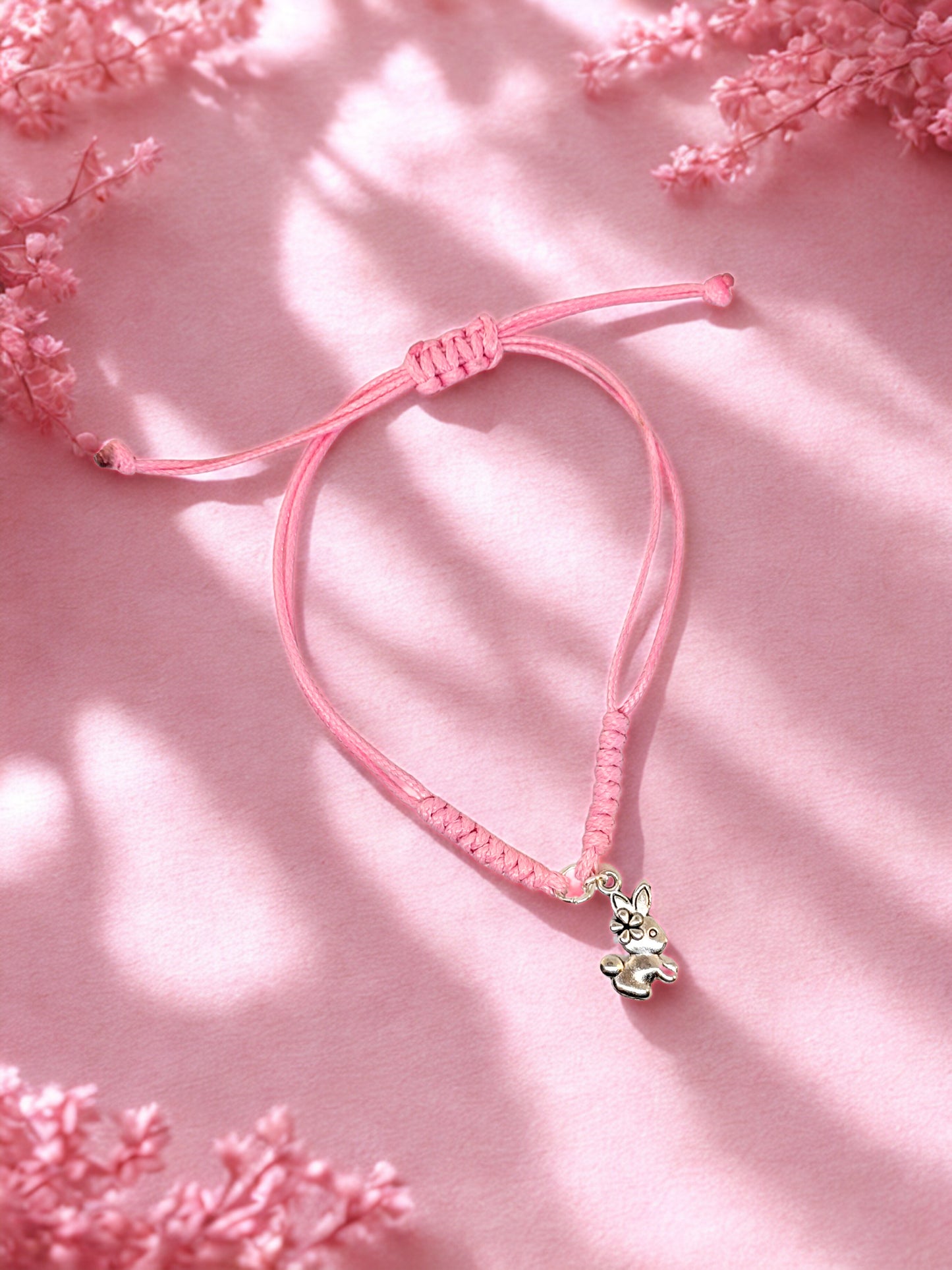 Pink bracelet with a small bunny charm on a pink background with floral elements