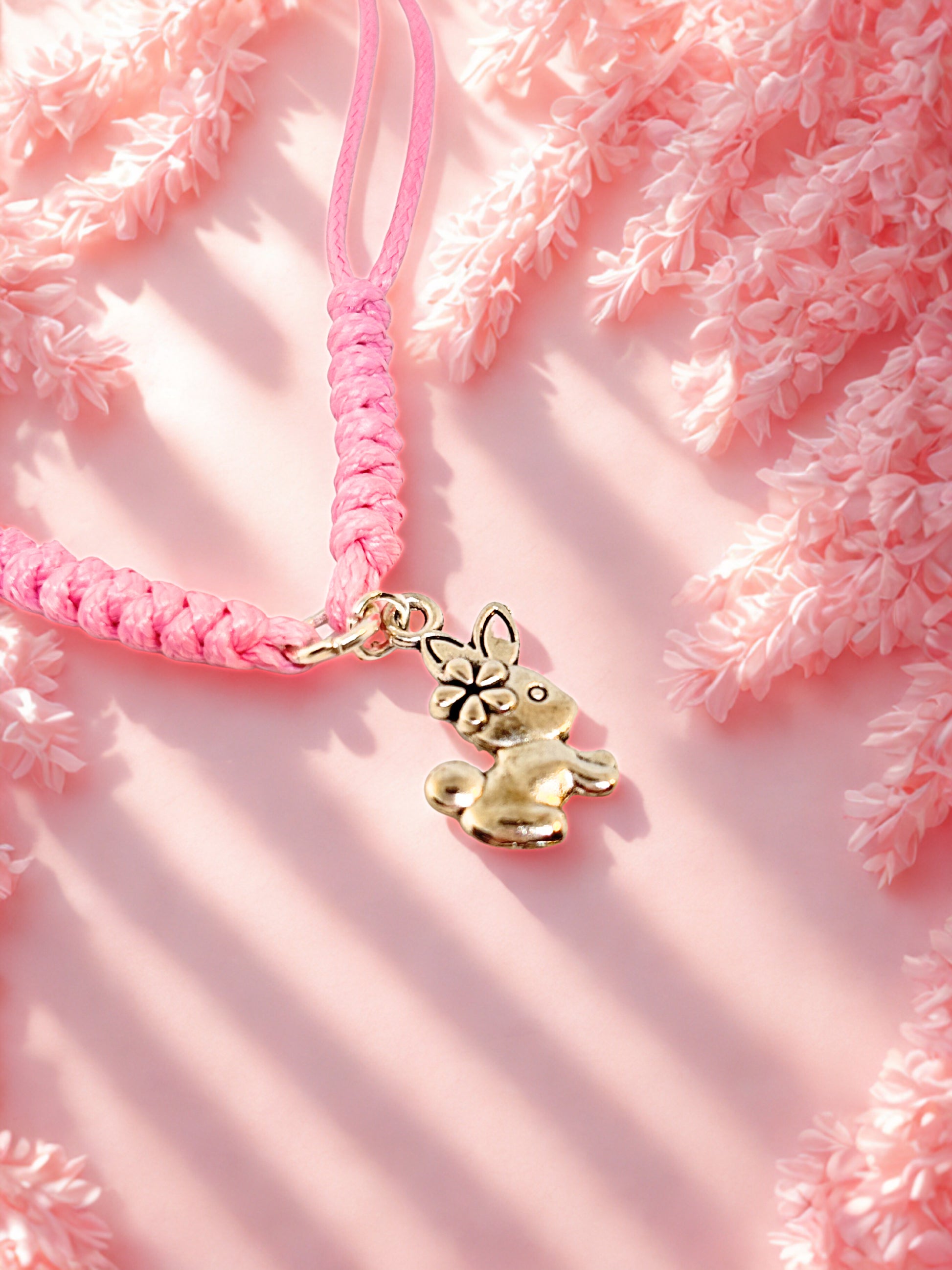 Pink braided bracelet with a silver bunny charm on a pink fluffy background
