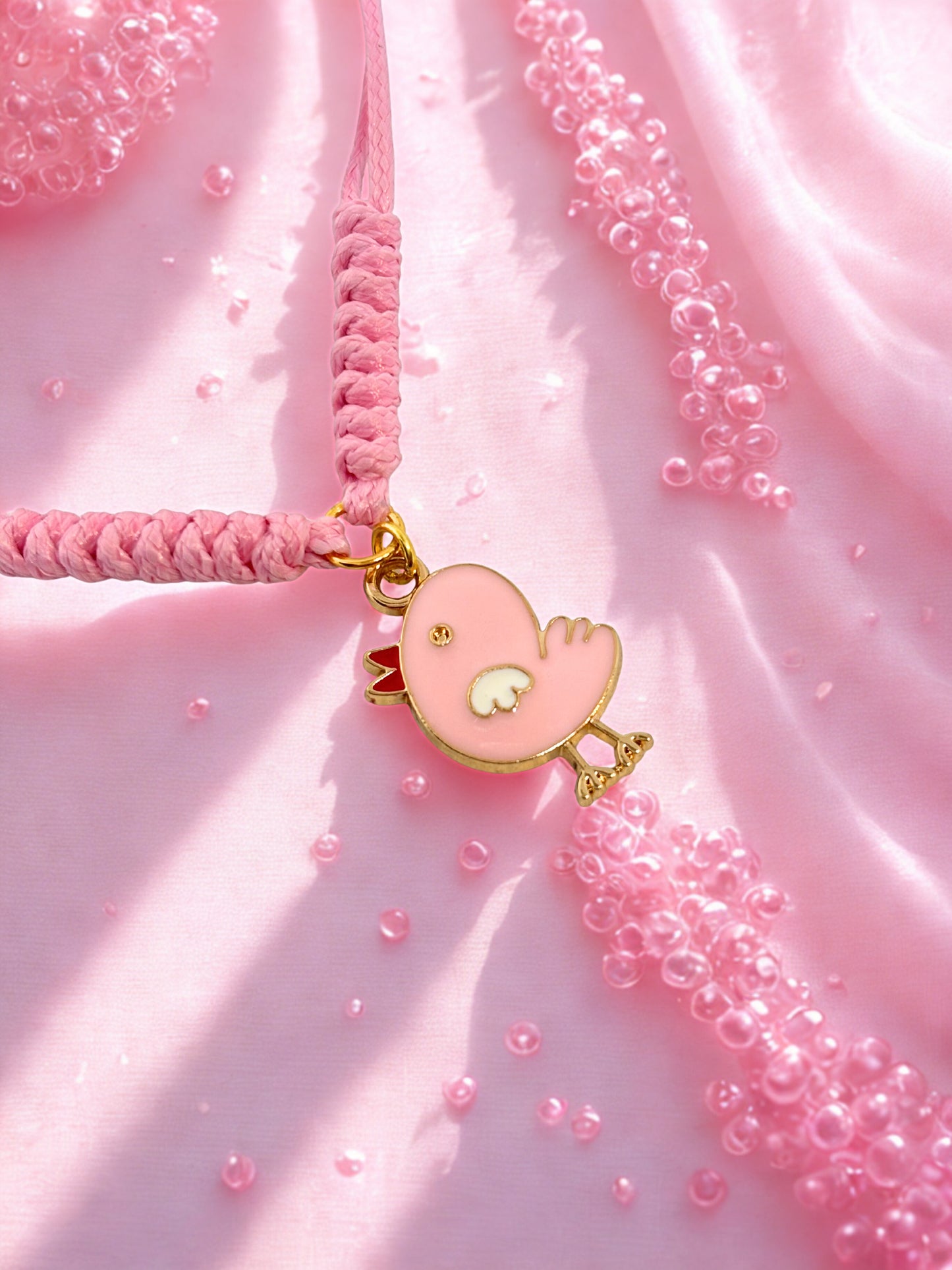 Pink cord bracelet with a chick shaped charm with on a pink fabric background