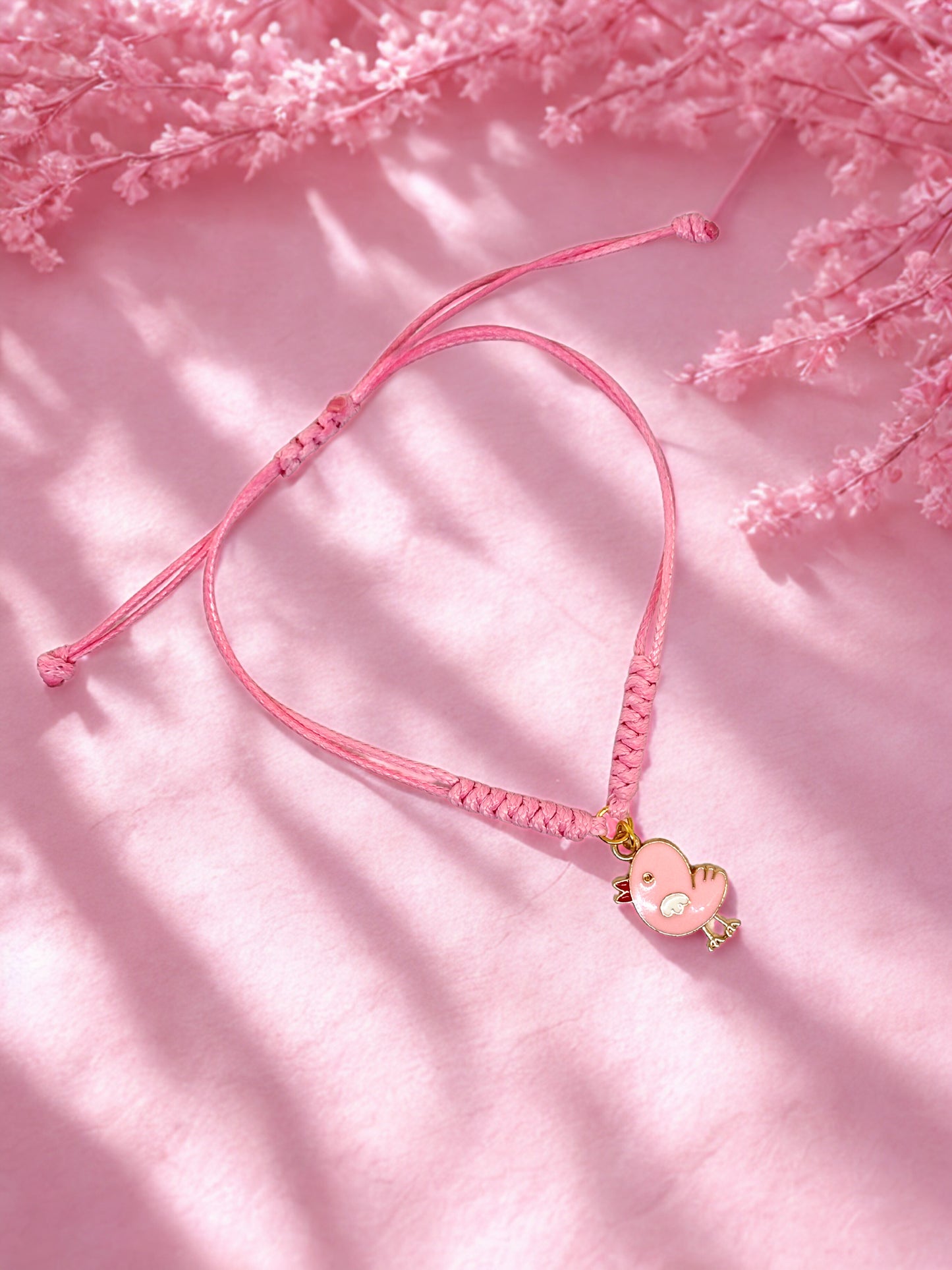 Pink bracelet with a chick charm on a pink background with floral elements