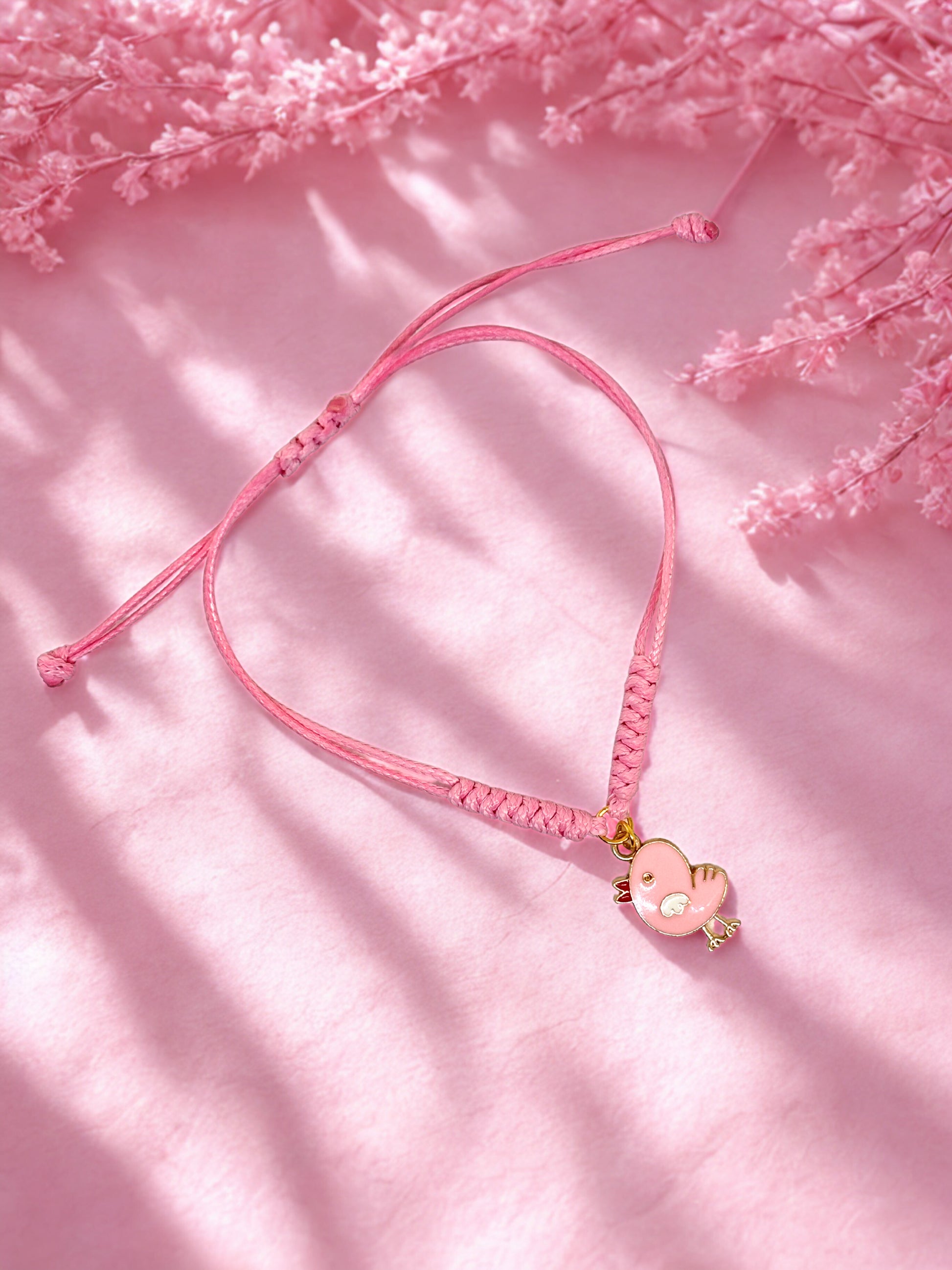 Pink bracelet with a chick charm on a pink background with floral elements