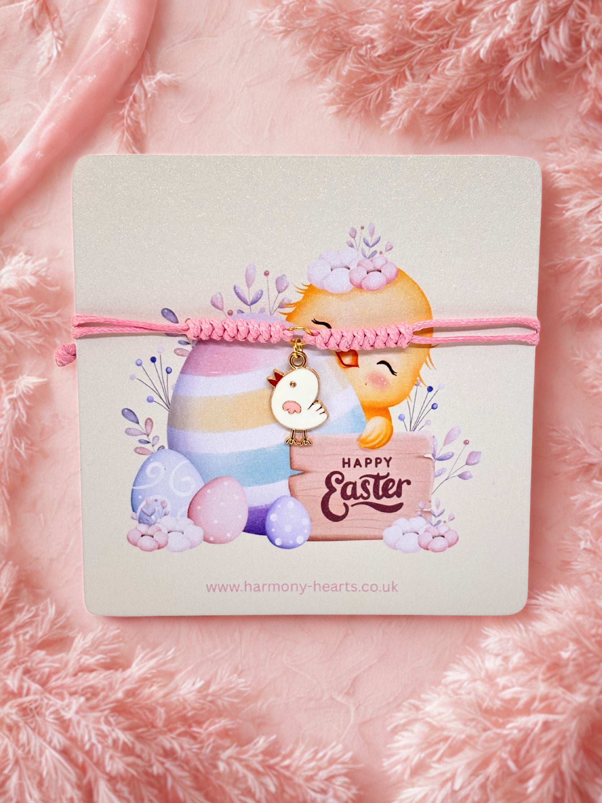 Pink cord bracelet with an Easter chick charm on an Easter illustrated card on a pink fluffy background