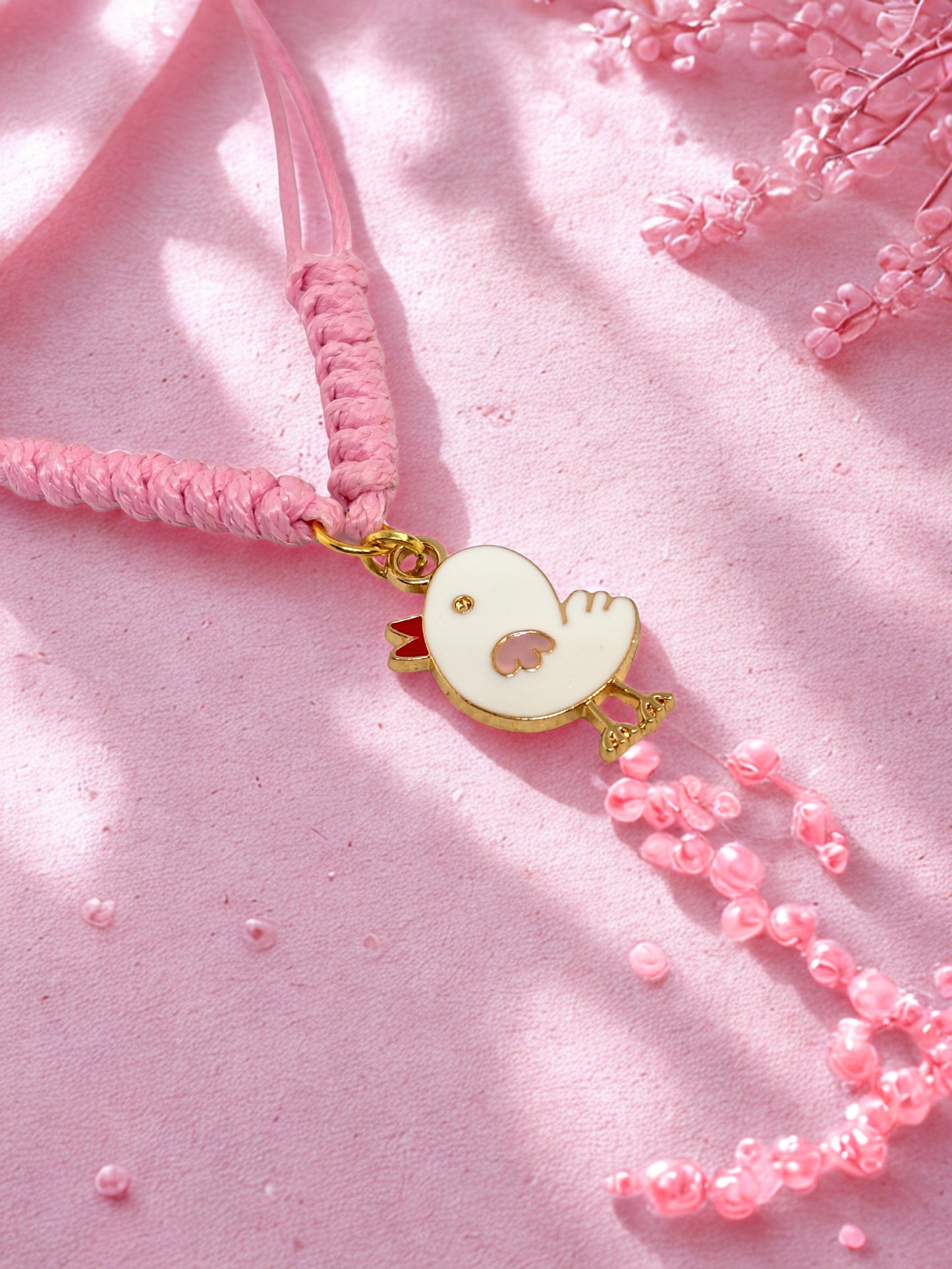Pink cord bracelet with a chick charm on a pink fabric background
