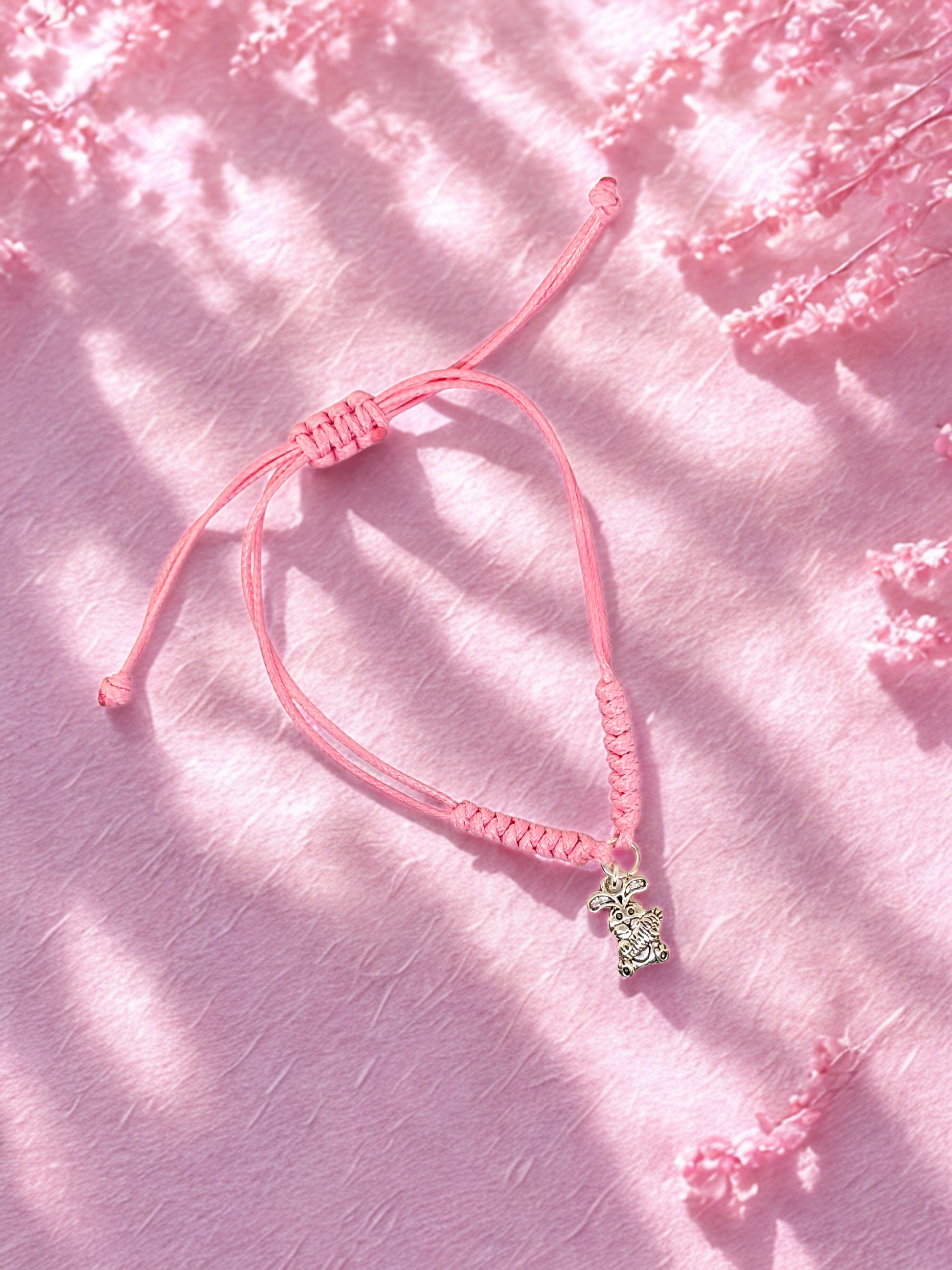 Pink bracelet with a small bunny charm on a pink textured background