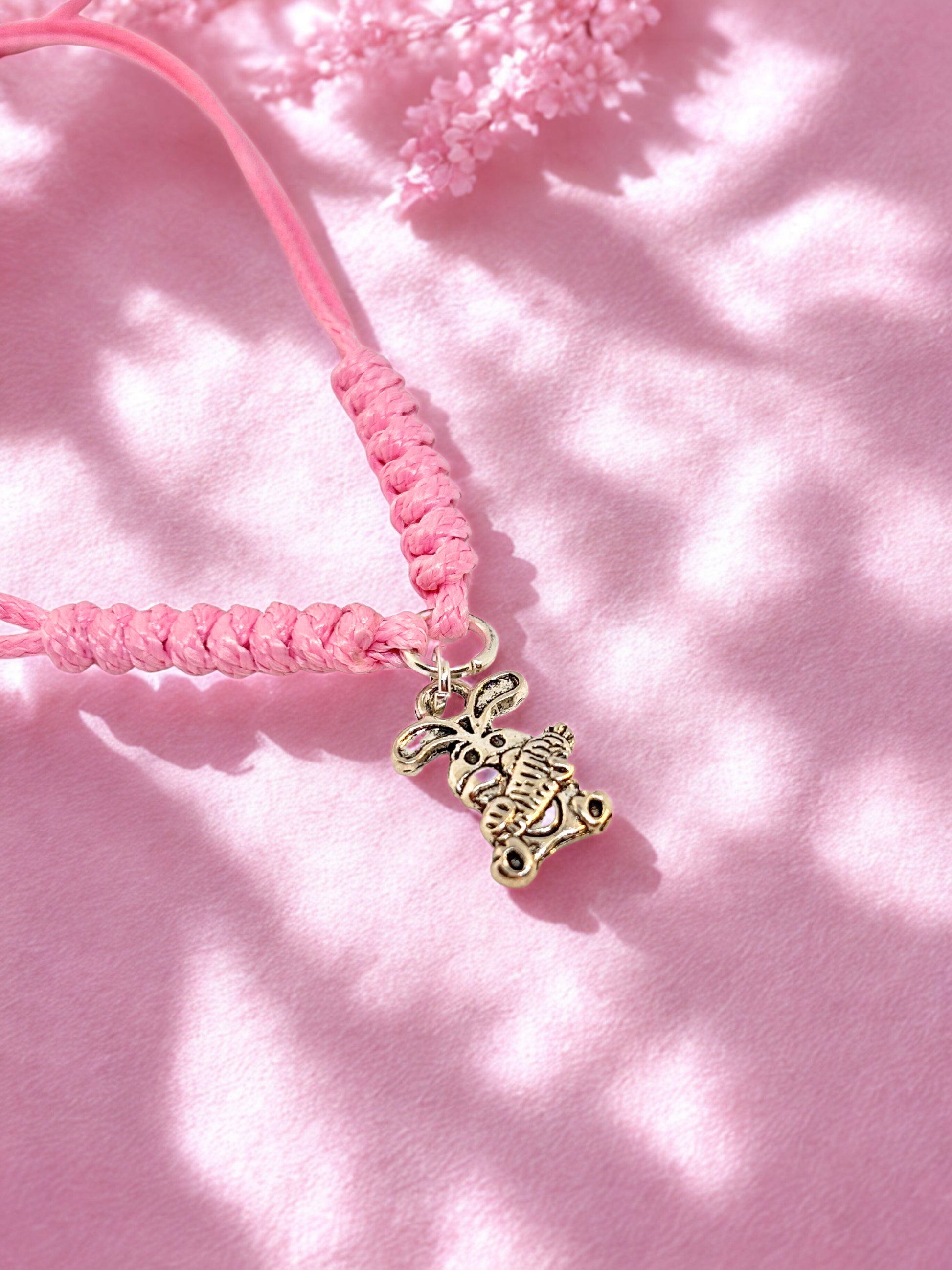 Pink cord bracelet with a silver bunny charm on a pink background