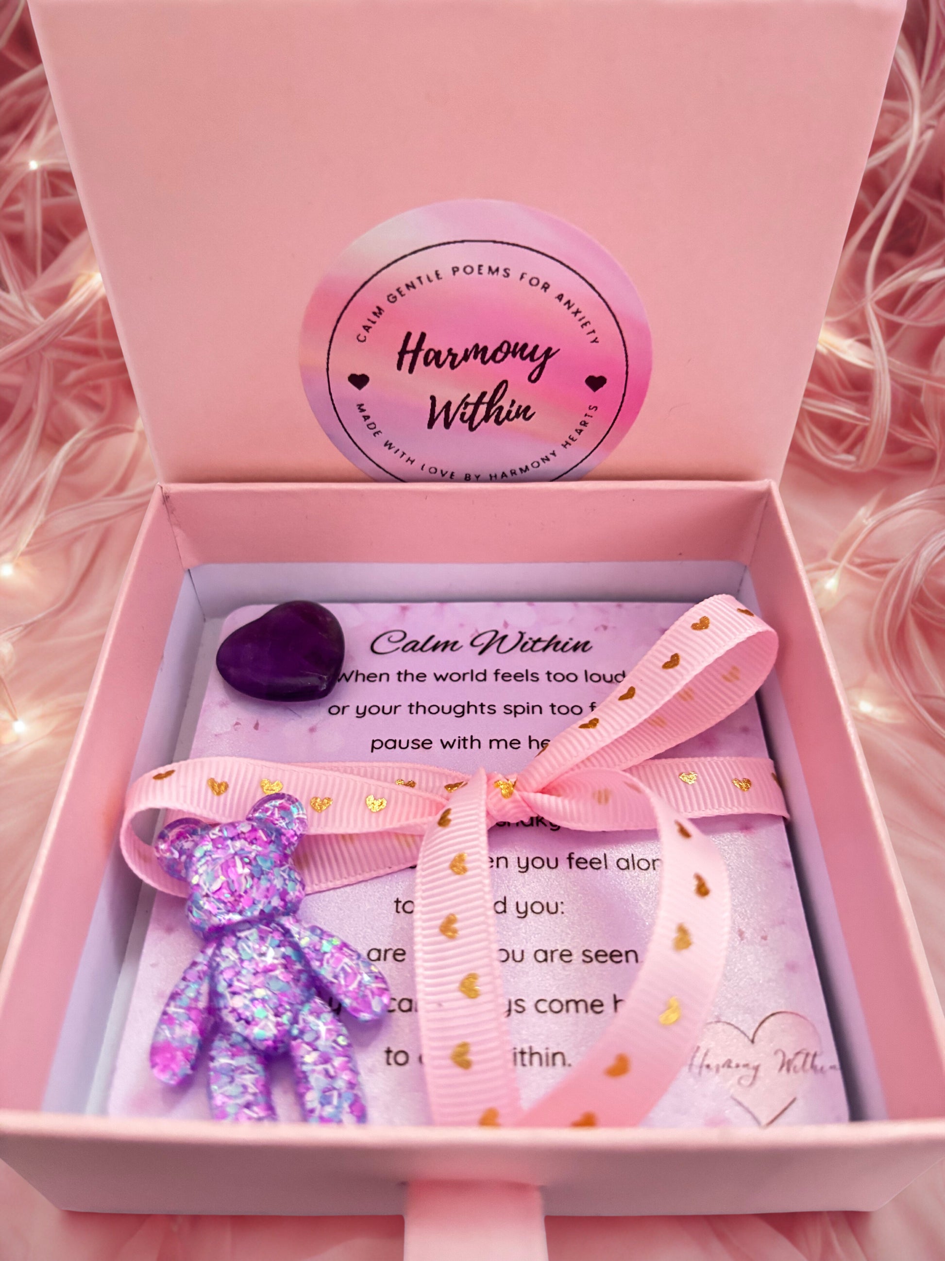 Pink gift box with a teddy bear, card, and heart-shaped object on a pink background.