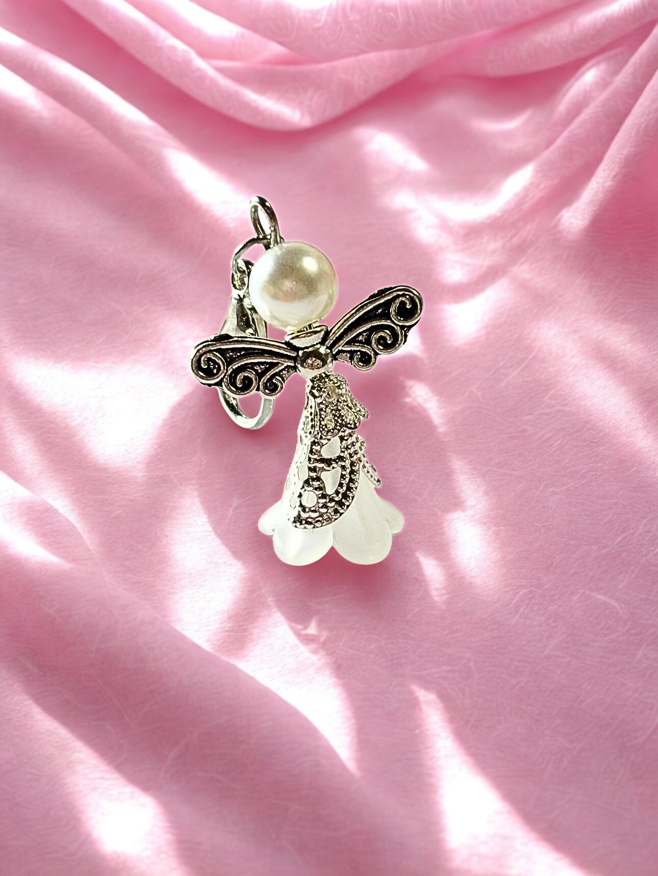 Decorative angel charm with pearl and floral design on a pink fabric background