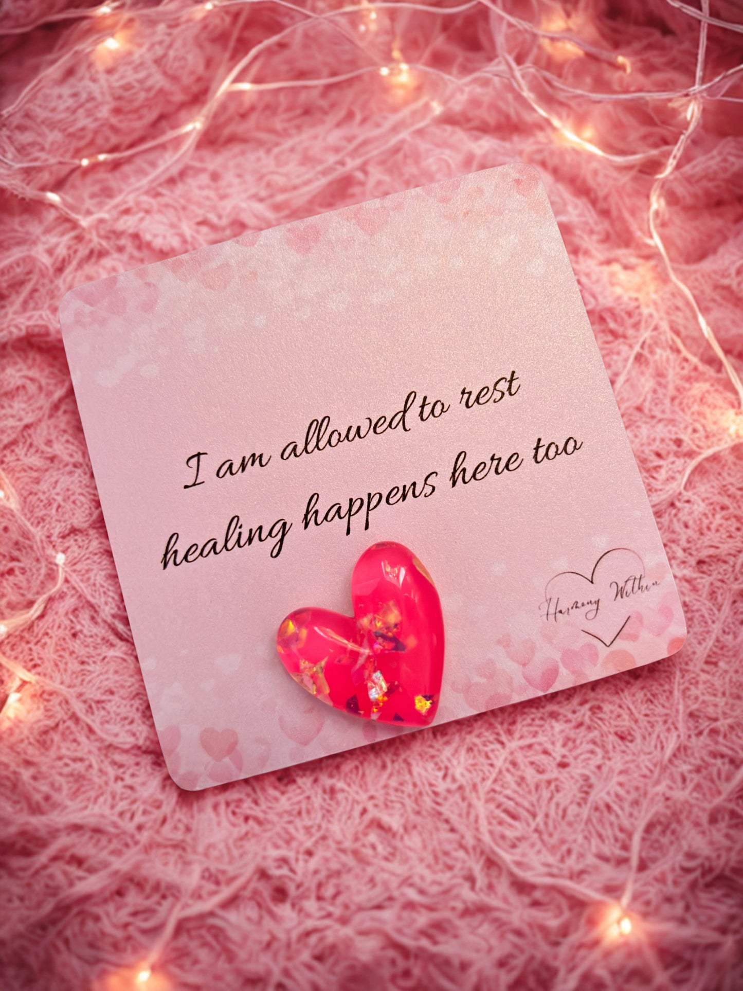 Card with a heart and inspirational message on a pink textured background with string lights.