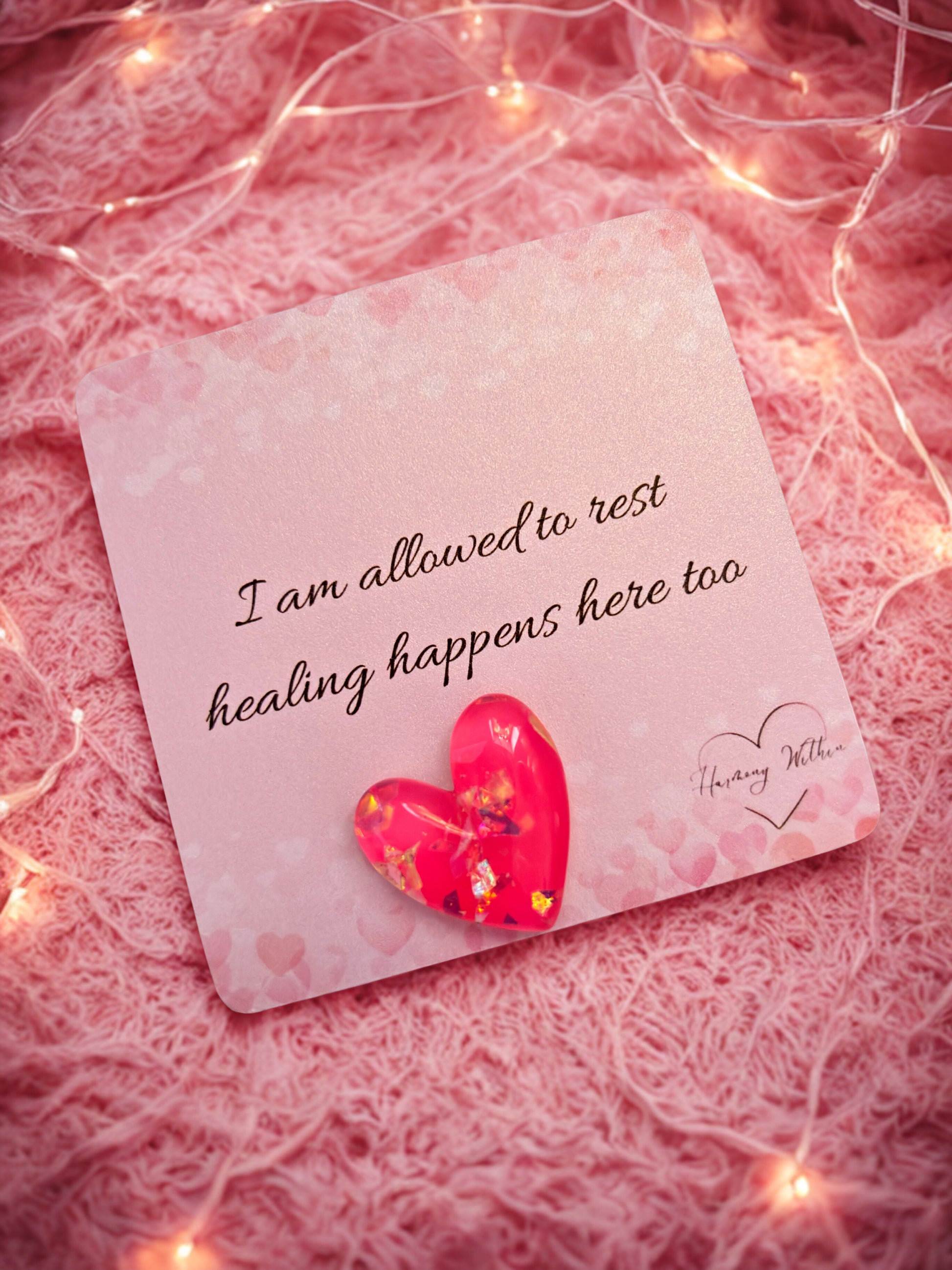 Card with a heart and inspirational message on a pink textured background with string lights.