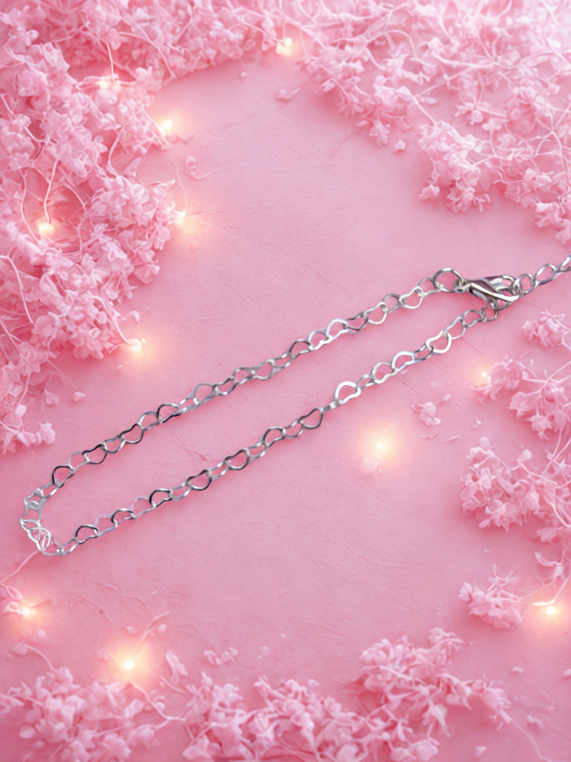 Silver heart-shaped chain necklace on a pink background with floral decorations