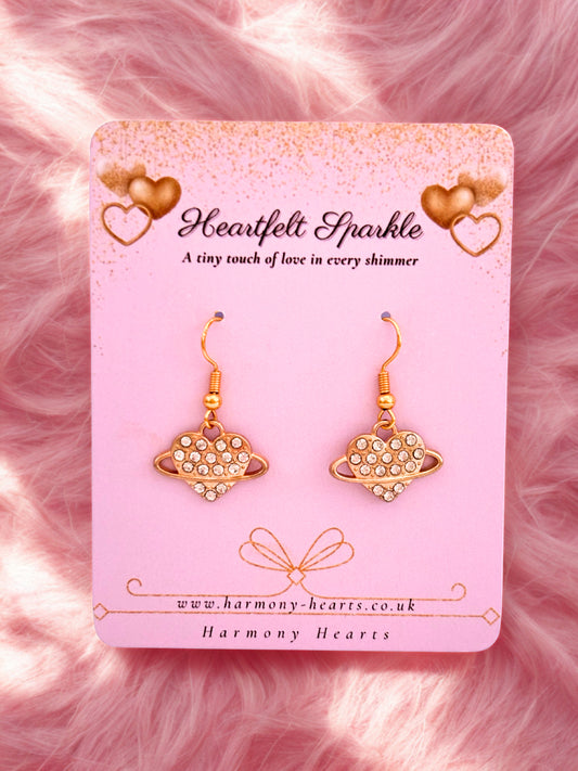 Gold earrings on a 'Heartfelt Sparkle' branded card against a pink fluffy background