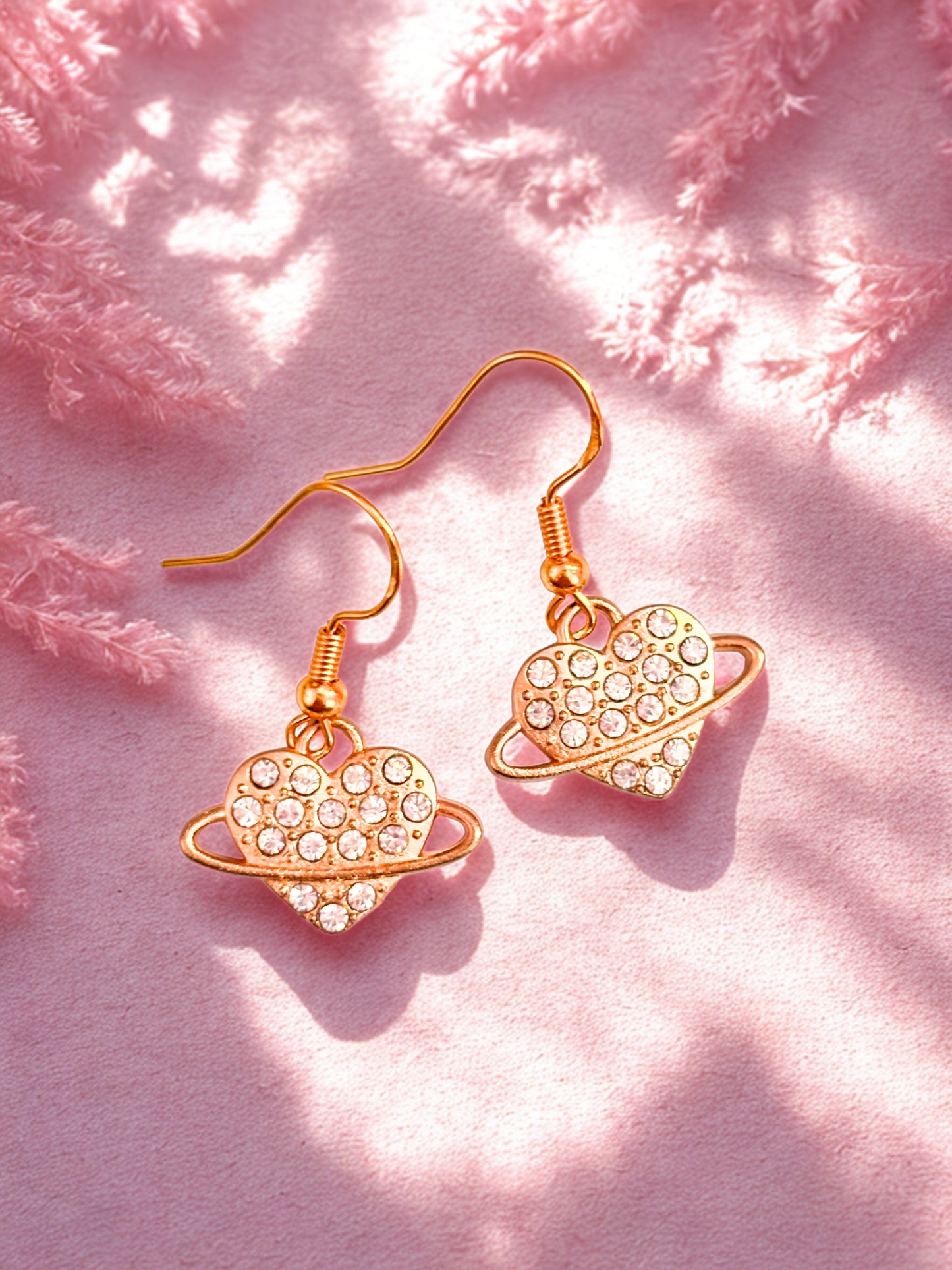 Heart-shaped earrings with gold and pink design on a pink textured background