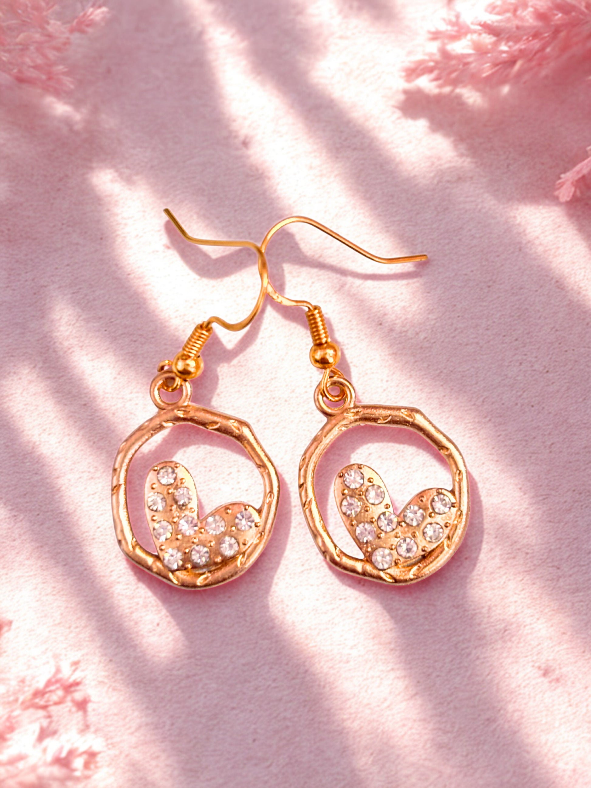 Gold heart earrings on a pink textured background