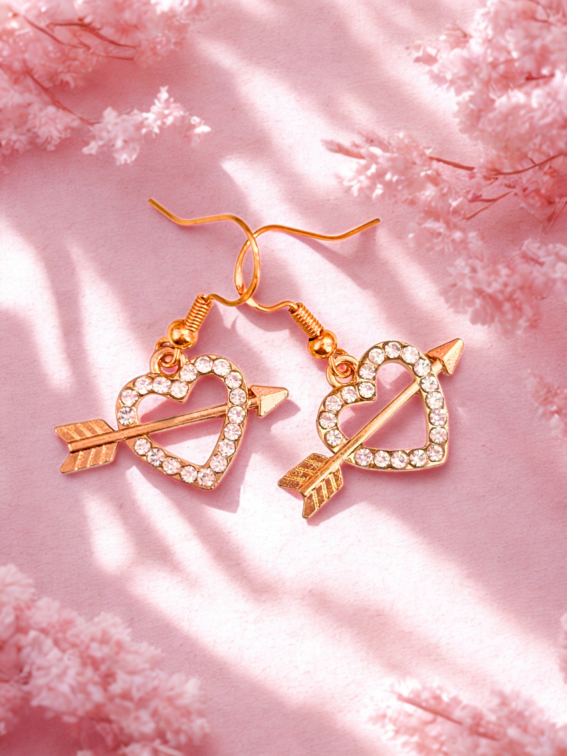 Rose gold heart and arrow earrings on a pink fabric background