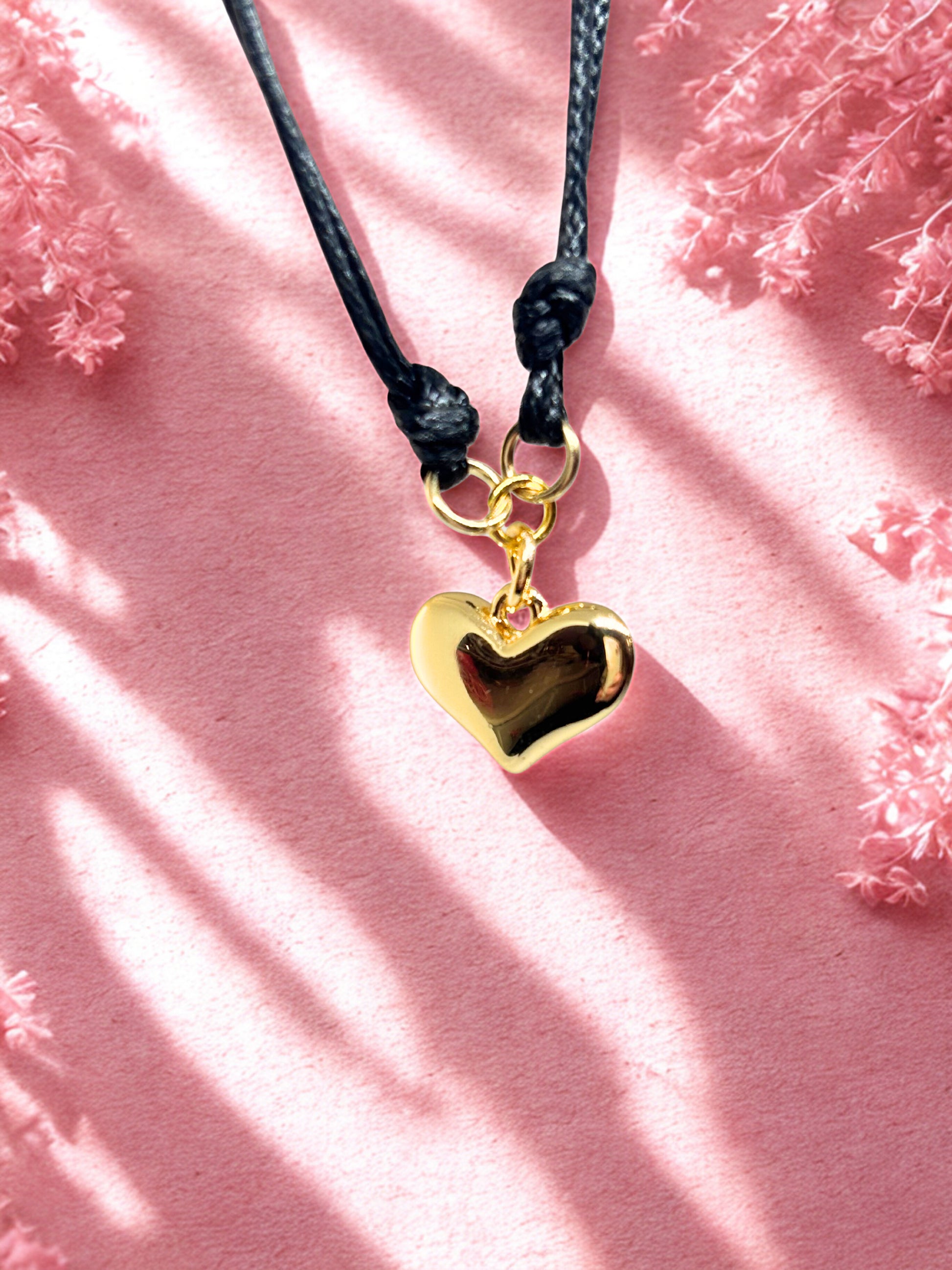 Gold heart-shaped charm on a black cord against a pink floral background