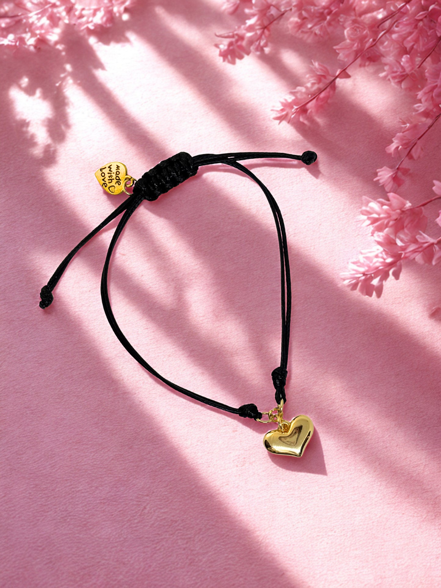 Black cord bracelet with gold heart charm on a pink floral background