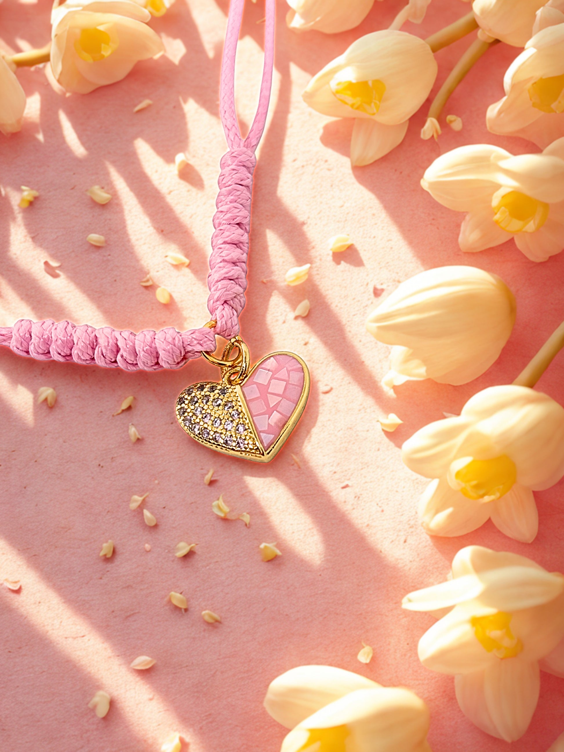 Pink and gold heart-shaped charm on a pink cord on a pink background with flowers