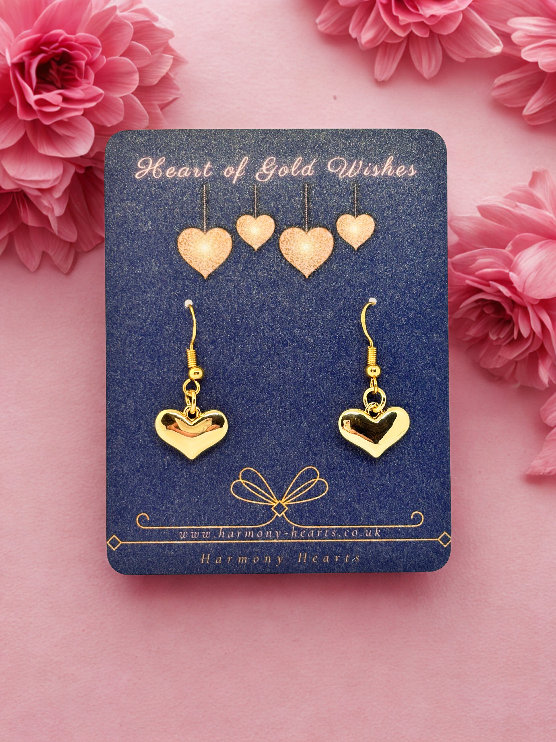 Gold heart-shaped earrings on a 'Heart of Gold Wishes' card with pink flowers in the background.