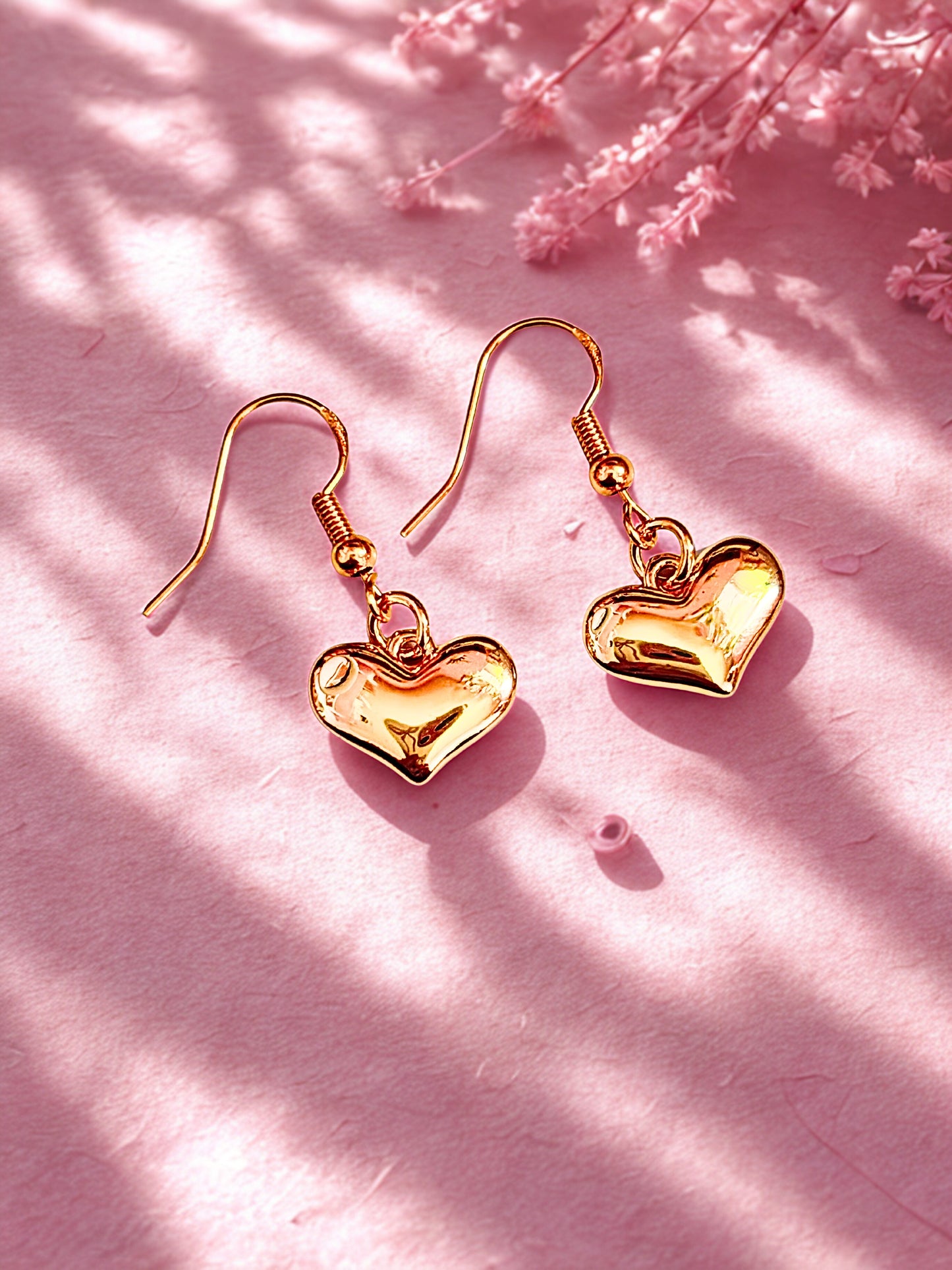 Gold heart earrings on hooks  laid on a pink decorative surface