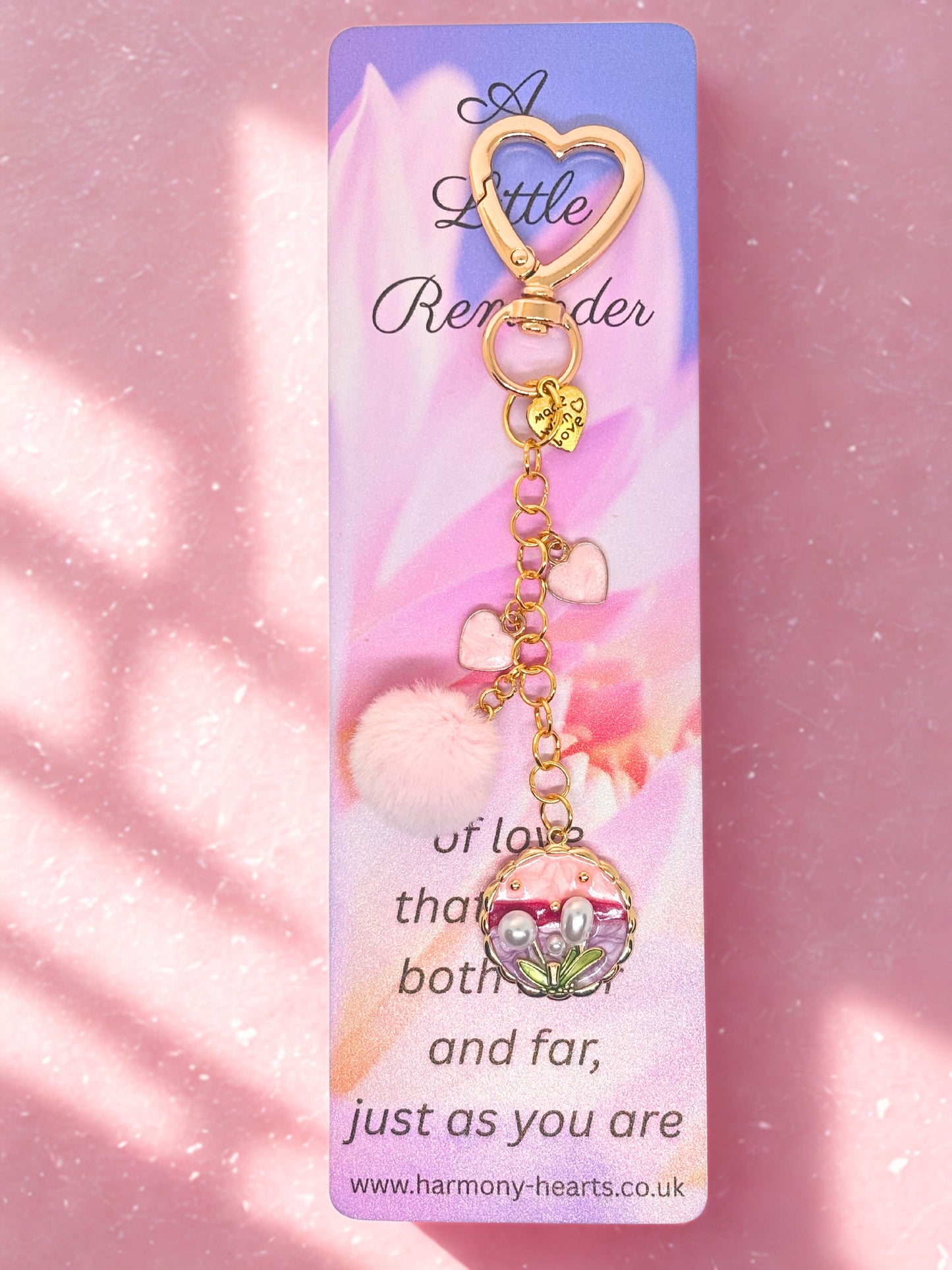 Heart-shaped keychain bag charm with floral design on a 'Harmony Hearts' branded card against a pink background.