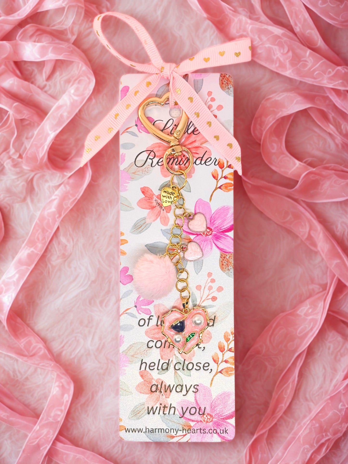 Decorative keychain bag charm with floral design and pink ribbon on a pink fabric background