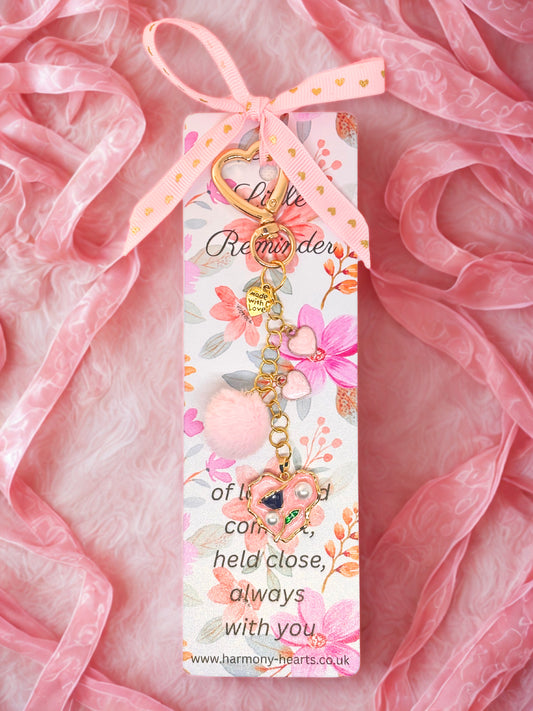 Decorative keychain bag charm with floral design and pink ribbon on a pink fabric background
