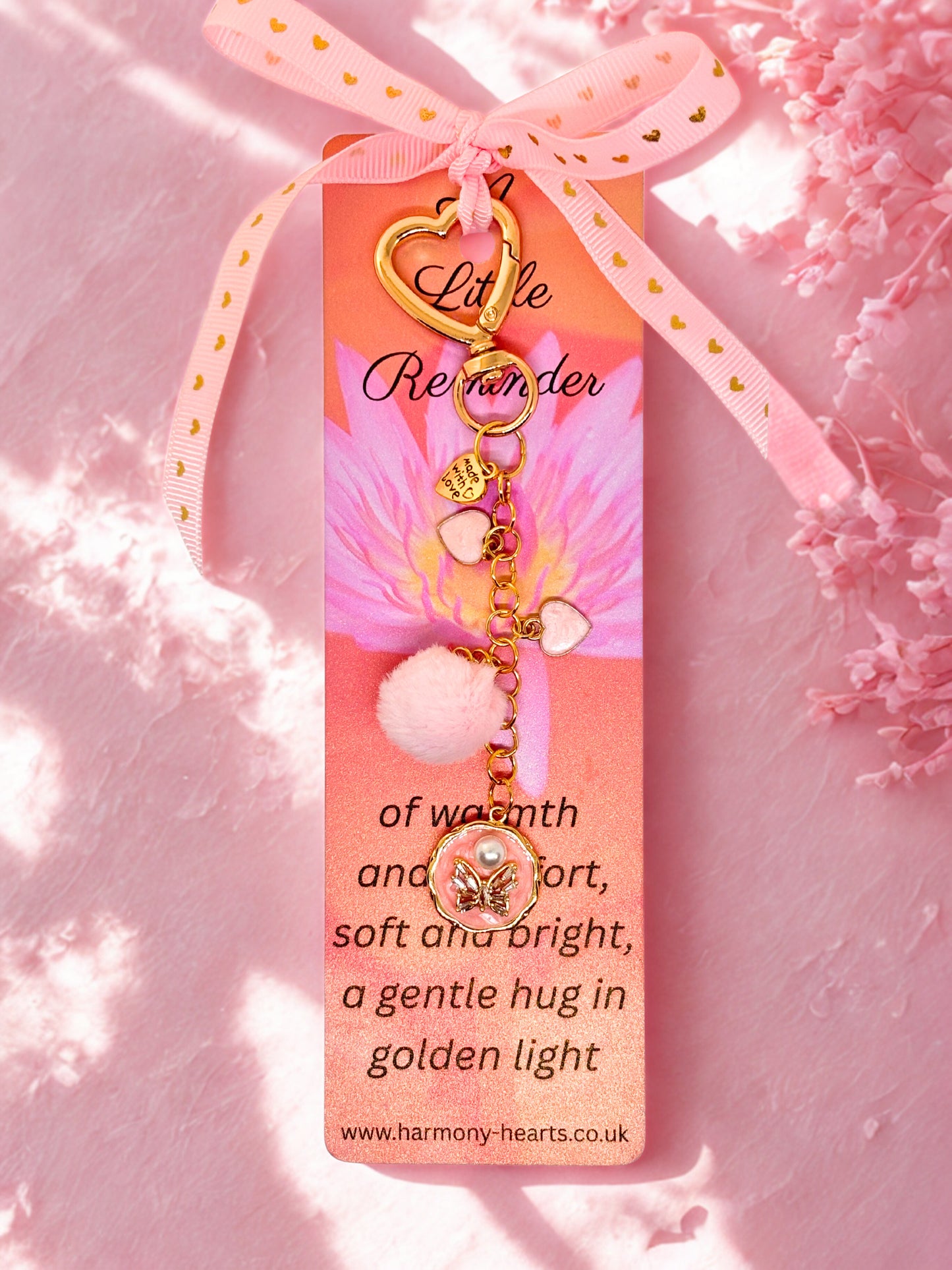 Decorative keychain bag charm  with gold charm and pink ribbon on a pink background