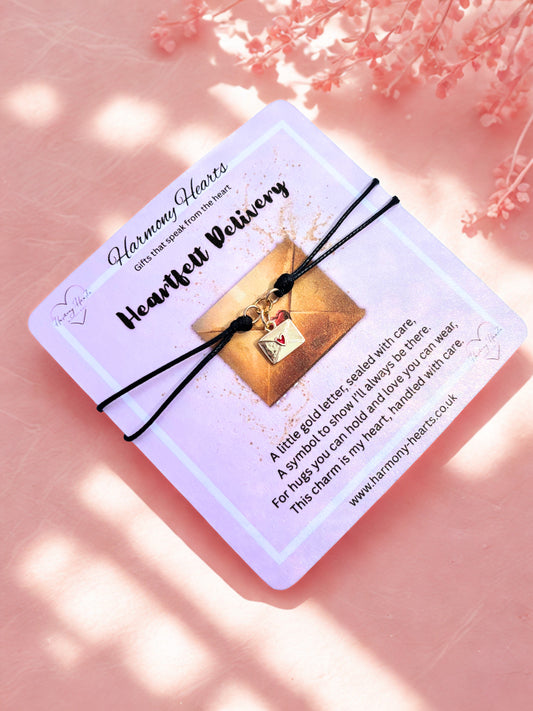 Bracelet with a gold envelope charm on a 'Harmony Hearts' card against a pink background