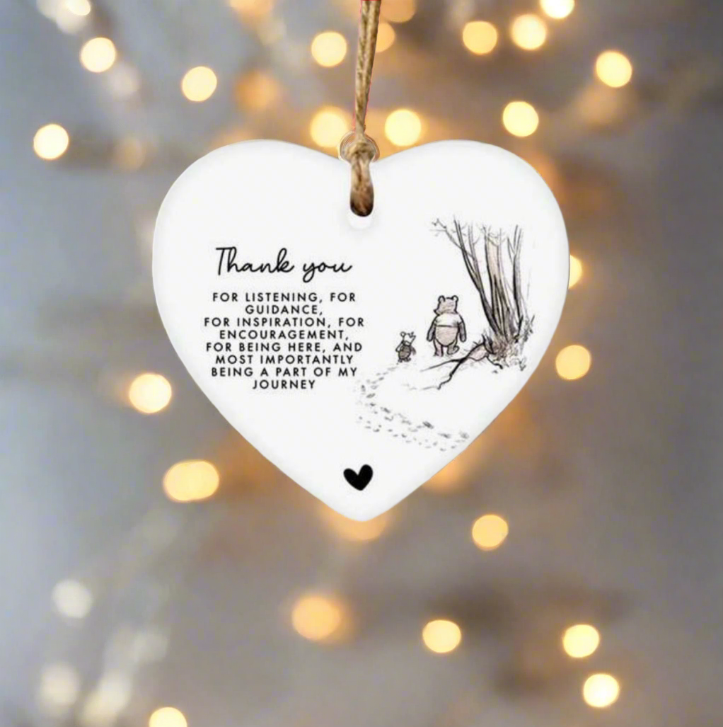 Heart-shaped hanging ornament with a message and illustration, against a blurred light background.