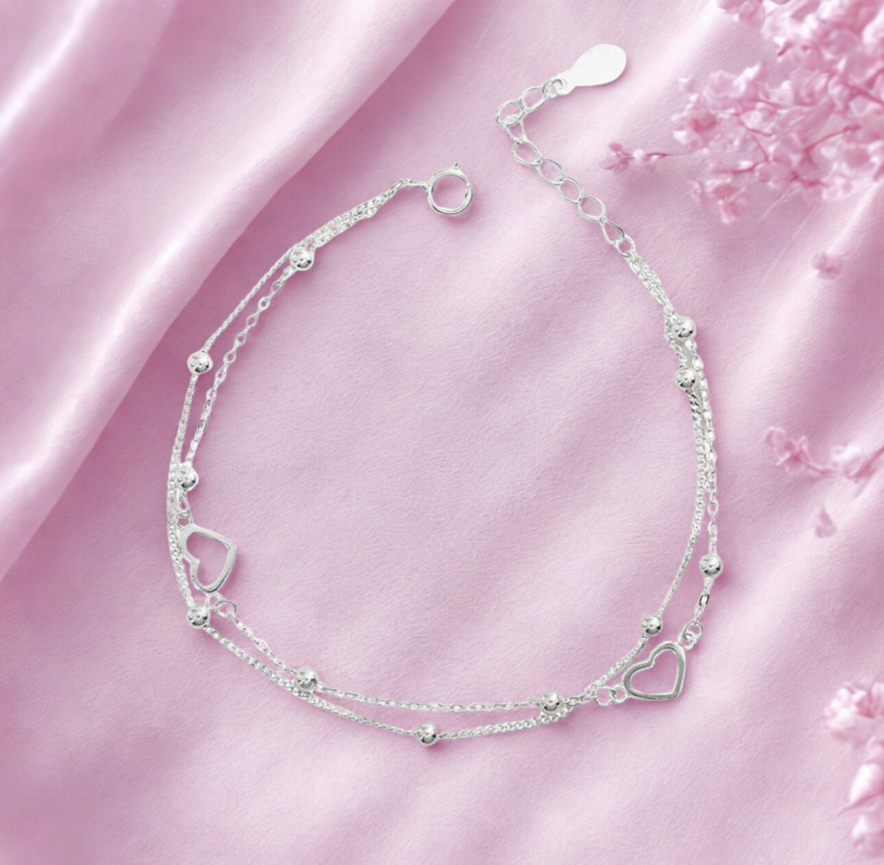 Silver bracelets with heart designs on a pink fabric background
