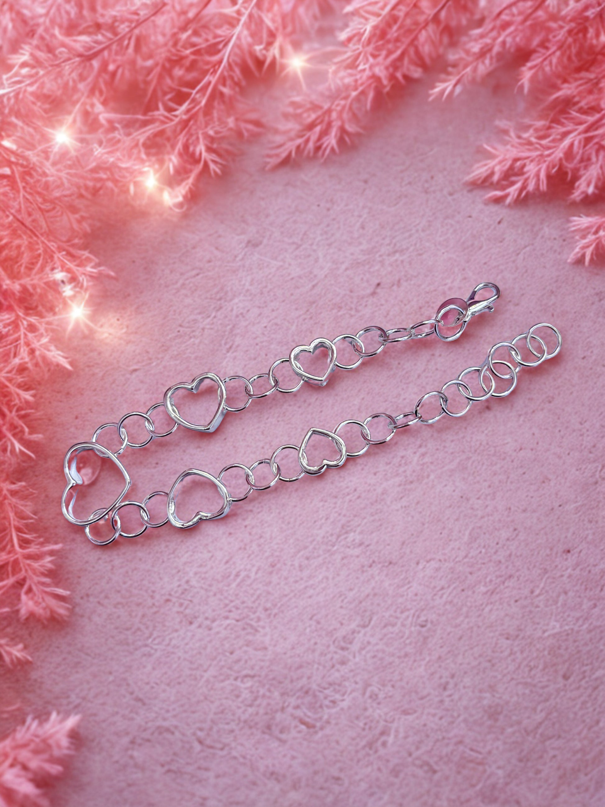 Silver heart-shaped bracelet on a pink background with decorative lights and pink flowers.