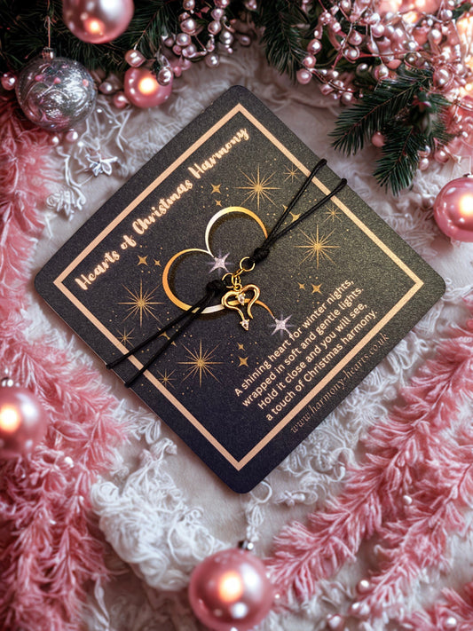 Gold heart charm on a black cord bracelet pn a festive poem card with festive decorations