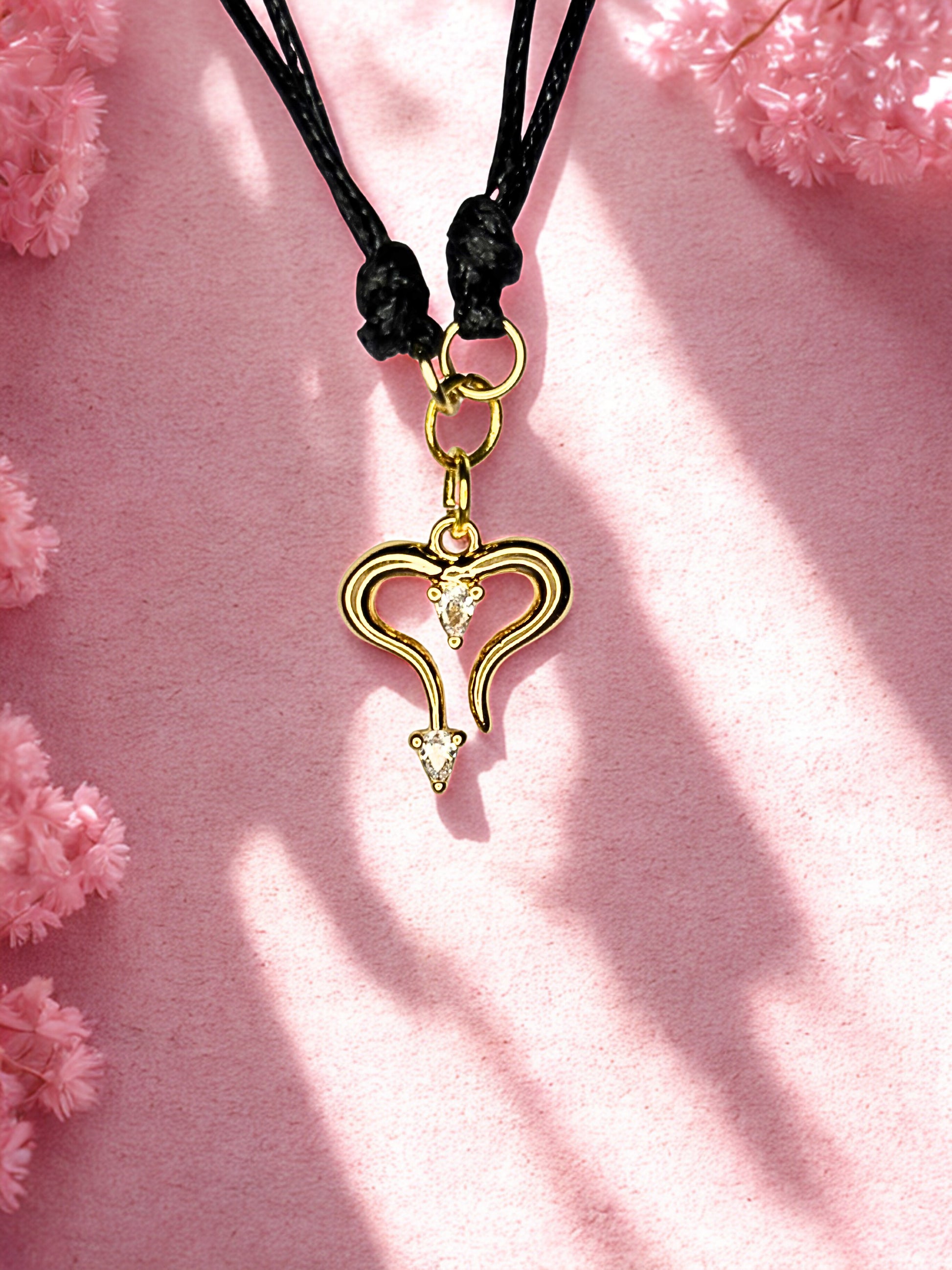 Gold heart-shaped charm on a black cord against a pink floral background