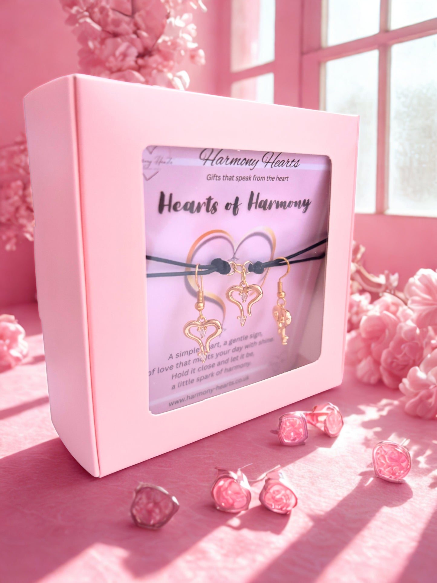 Pink jewelry box with heart bracelet and earrings with 'Hearts of Harmony' branding on a pink surface with decorative elements.