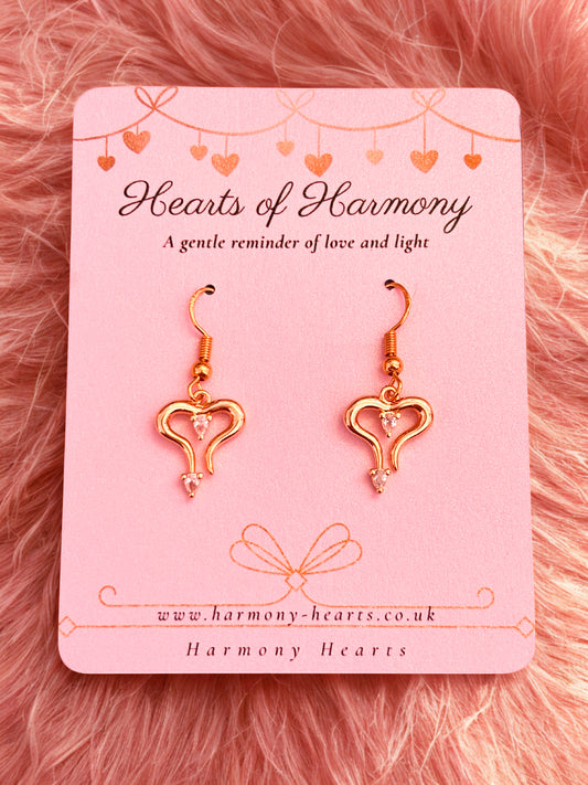 Heart-shaped earrings on a 'Hearts of Harmony' branded card against a pink fluffy background