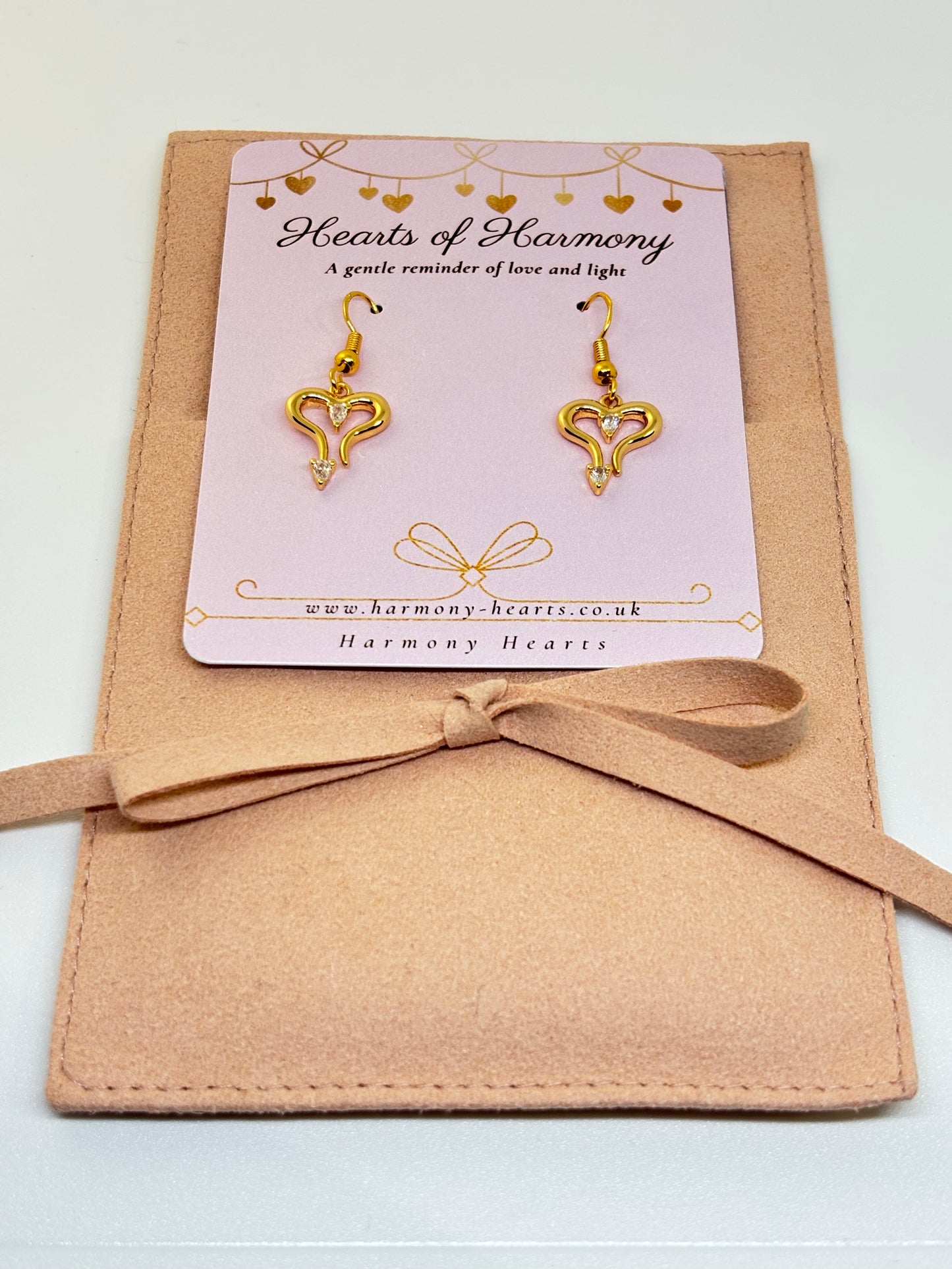 Gold heart-shaped earrings on a 'Hearts of Harmony' card with a beige ribbon.