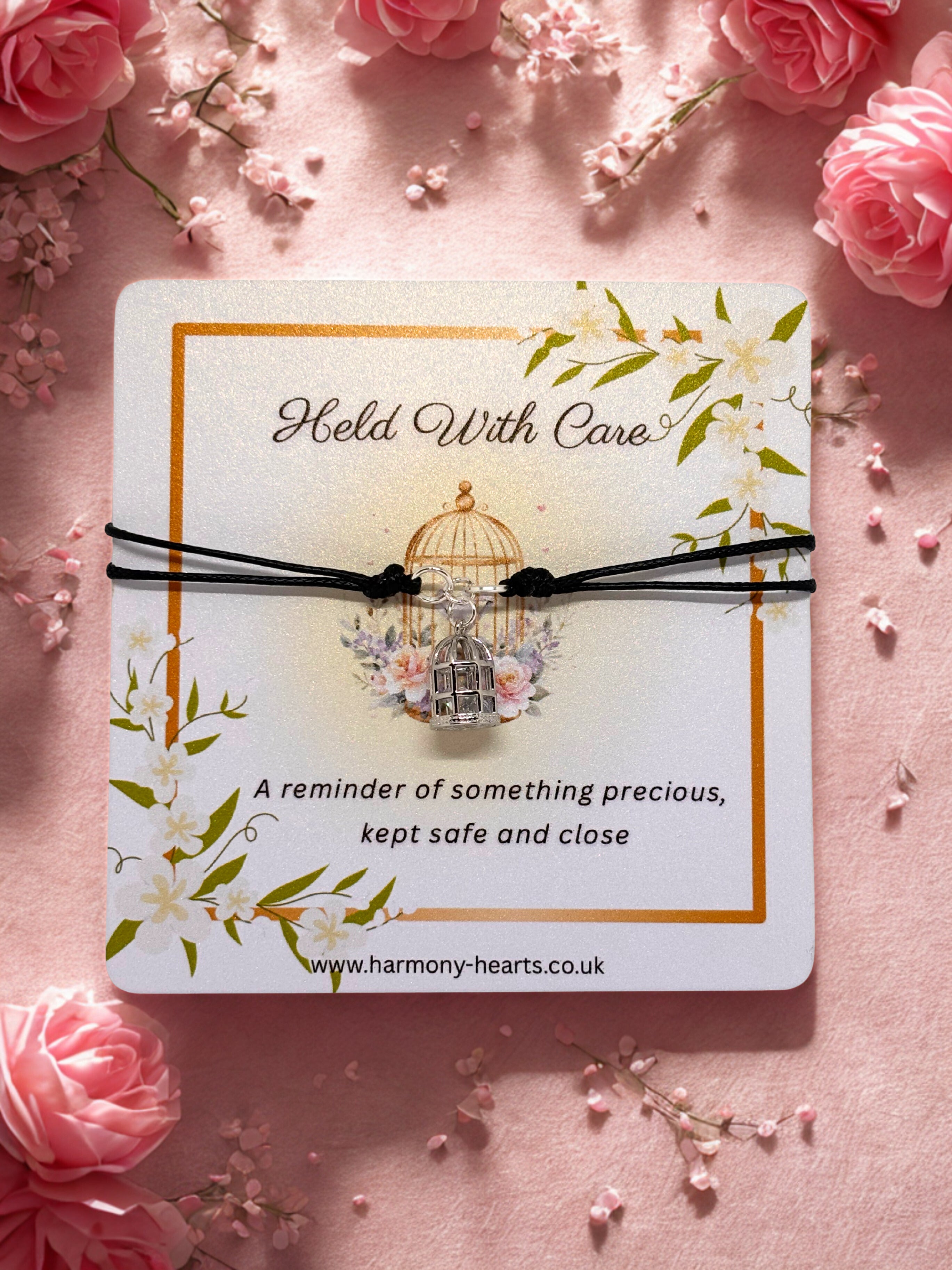 Card with a black cord charm bracelet with birdcage charm and decorative elements on a pink floral background