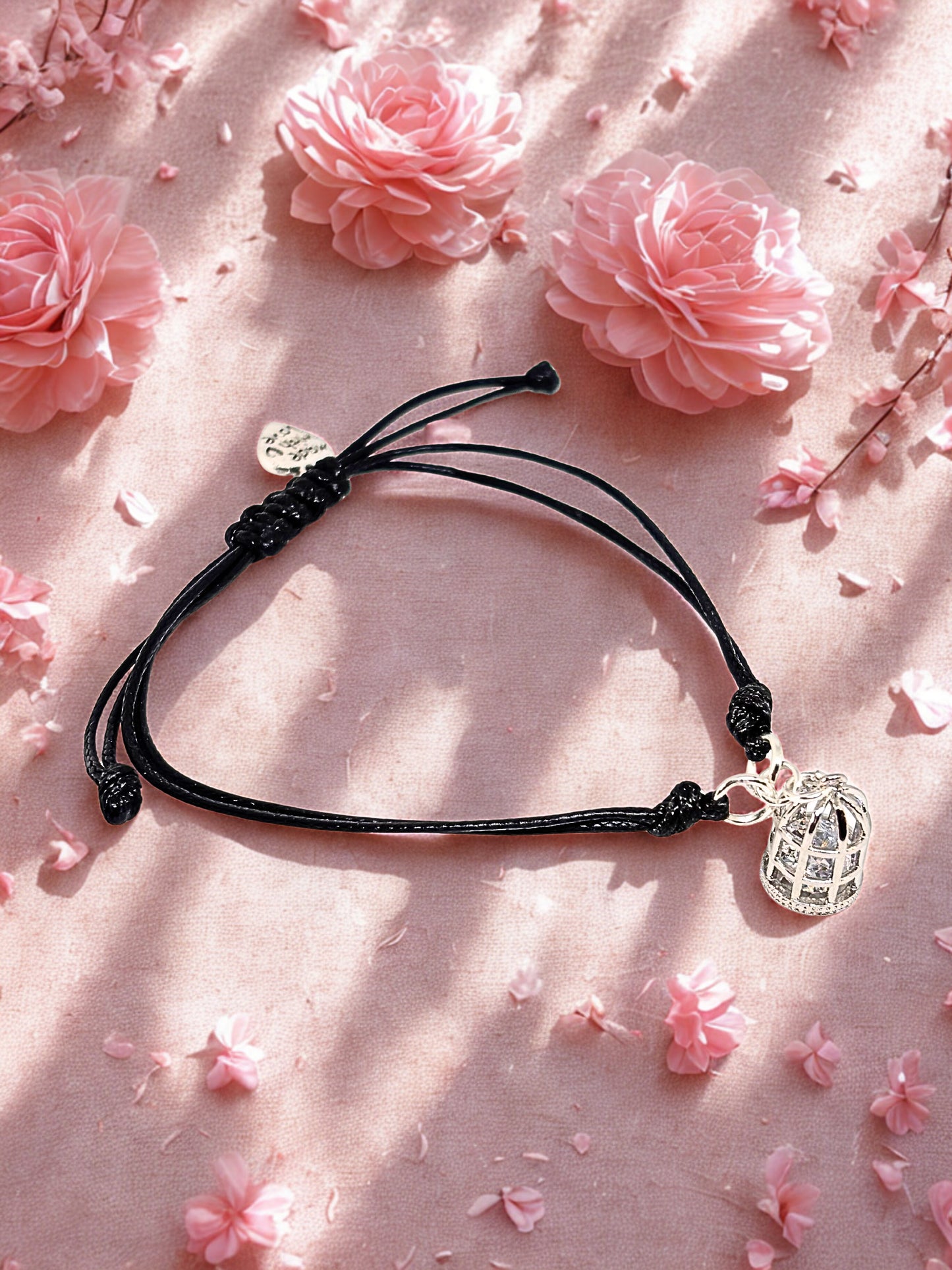 Black cord bracelet with a silver birdcage charm on a pink floral background